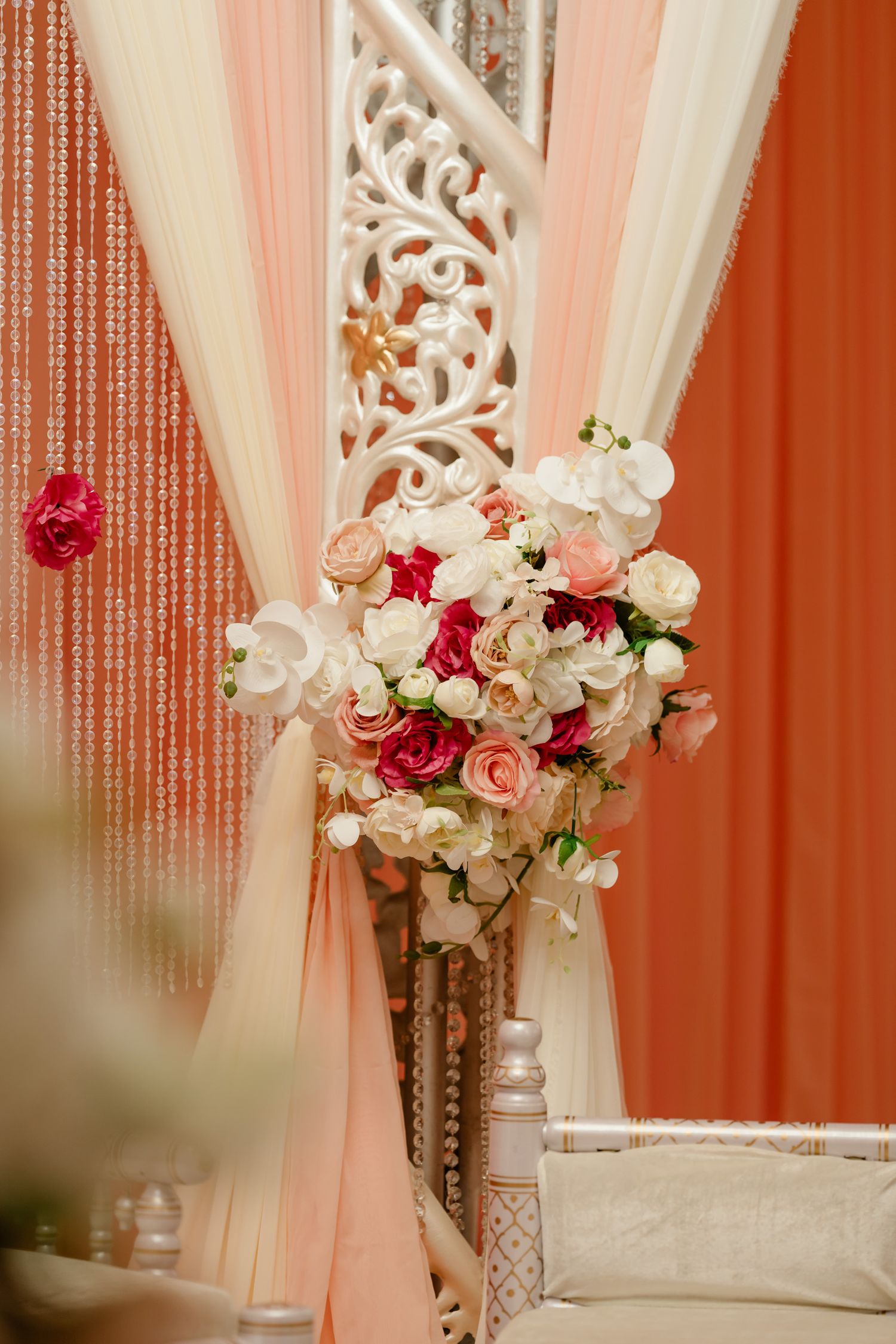 Elegant wedding decor with crystal curtains, white drapes, and pink and red rose floral arrangements.