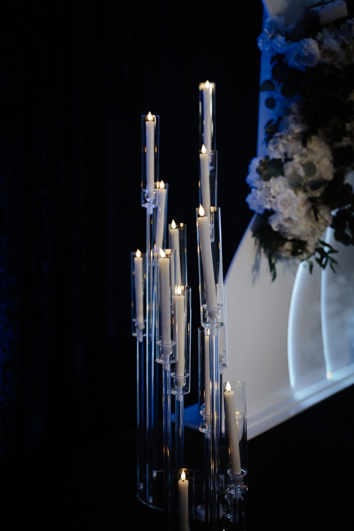 Tall white taper candles arranged in modern glass holders create an elegant wedding decoration display.