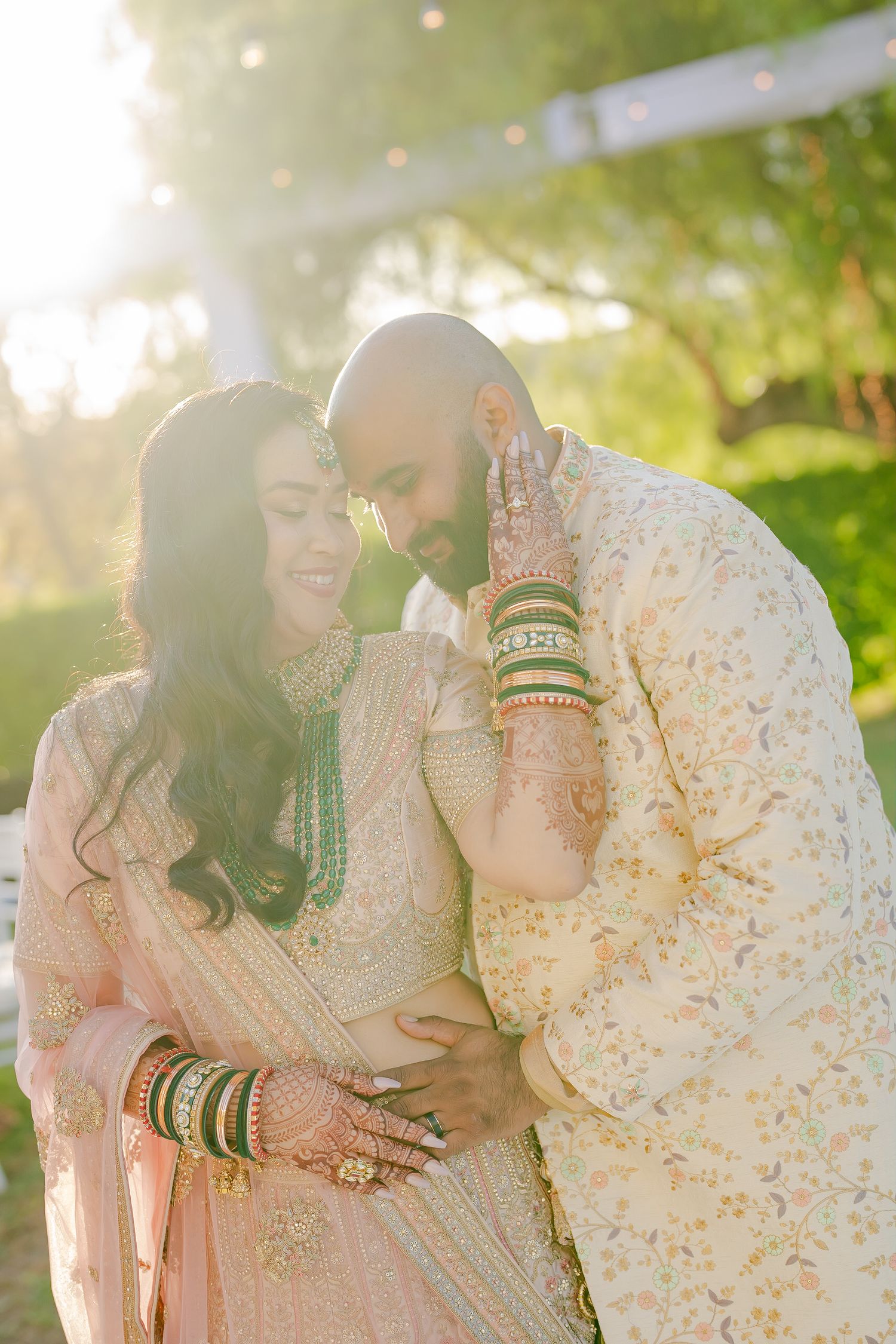 Couple in traditional South Asian wedding attire embracing in a sunlit garden setting.