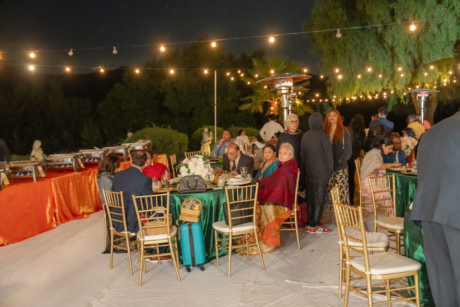 Panoramic view of an outdoor wedding reception with string lights and white chairs arranged under the night sky.