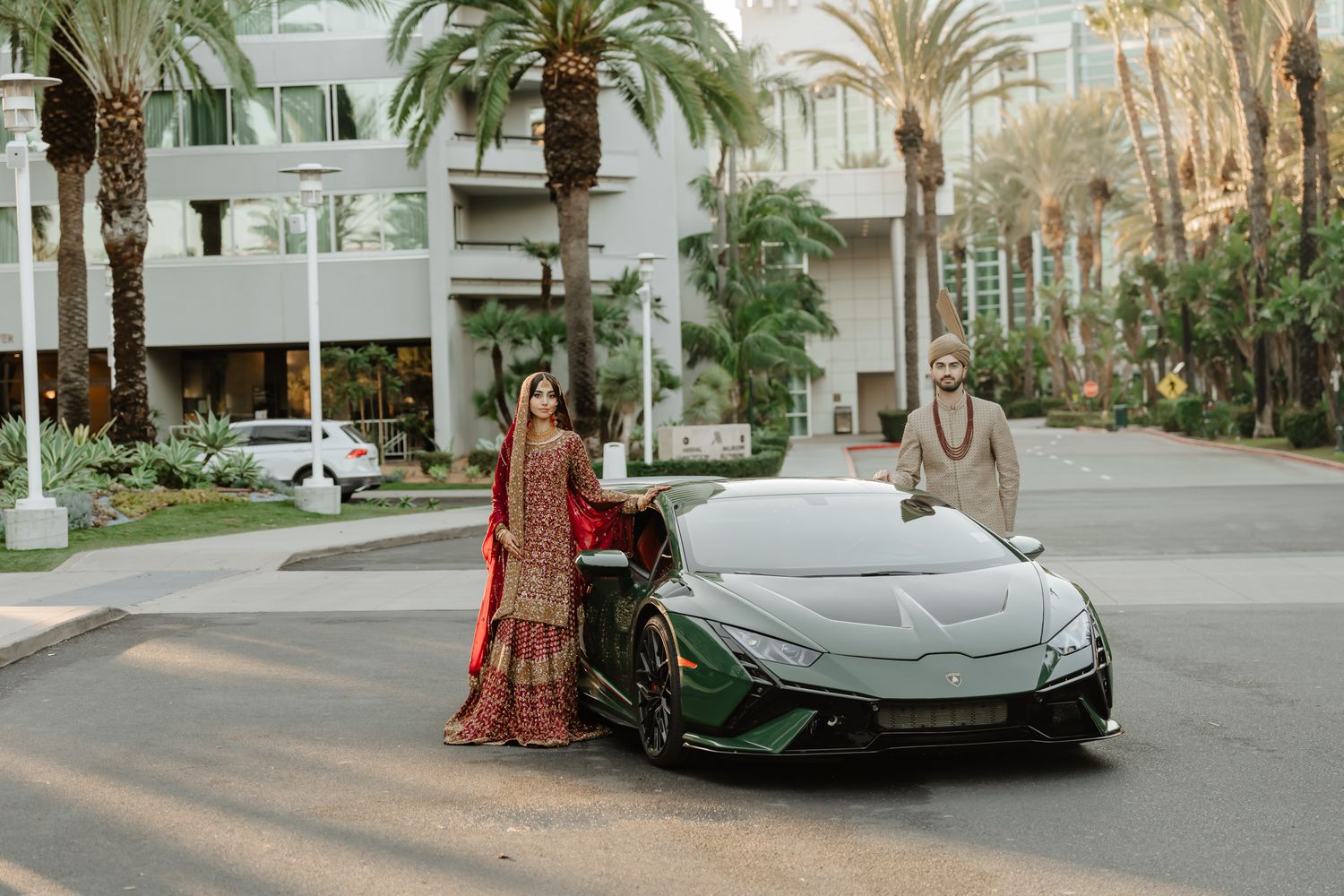 Luxury sports car parked in front of palm trees with traditional South Asian wedding attire.