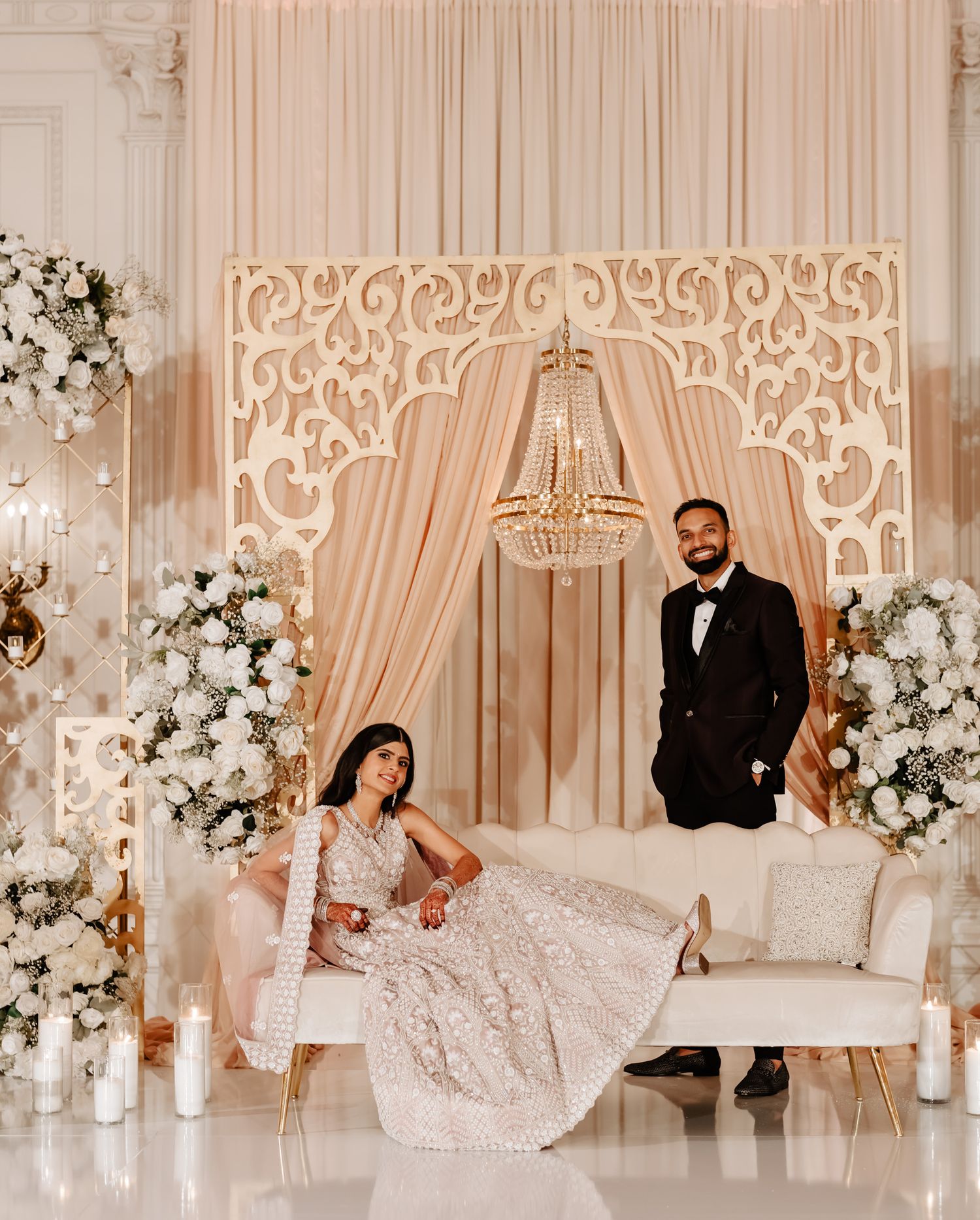Elegant wedding venue setup with white floral arrangements, crystal chandeliers, and draped fabric creating a romantic atmosphere.