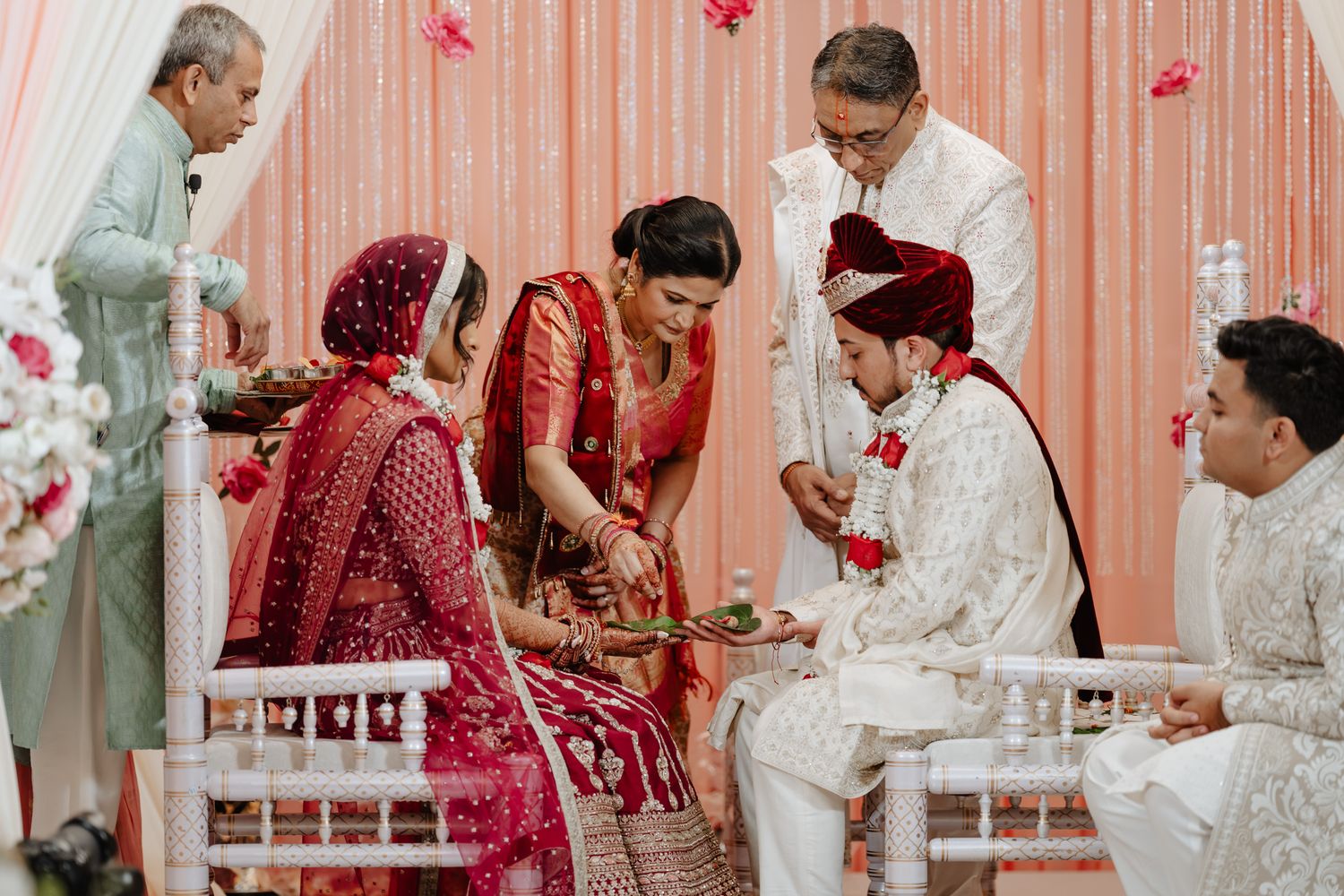 Traditional Indian wedding ceremony with guests gathered around in traditional attire with red and pink decor.