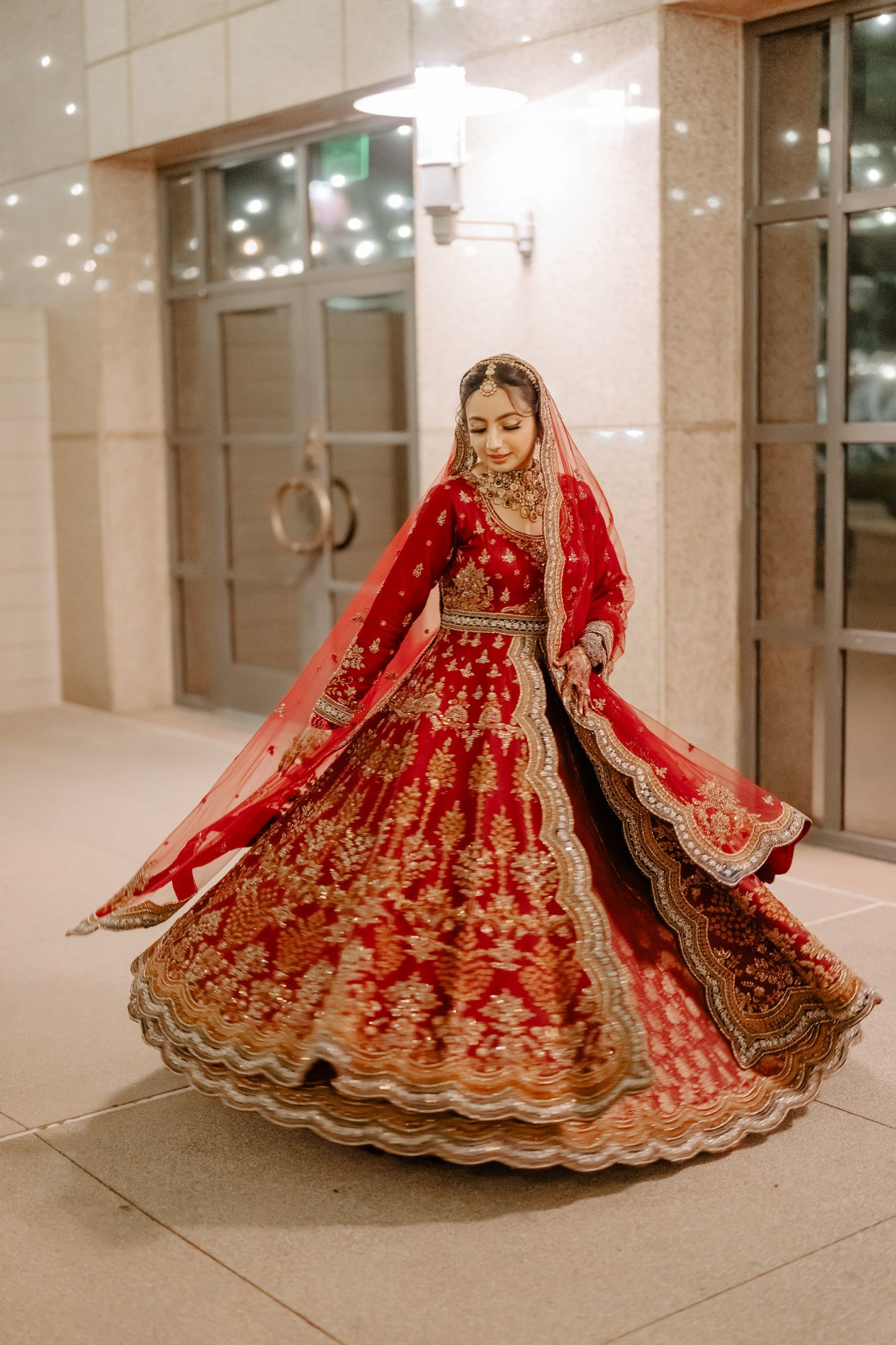 A bride in a red and gold lehenga twirls to show off the flowing fabric of her dress.