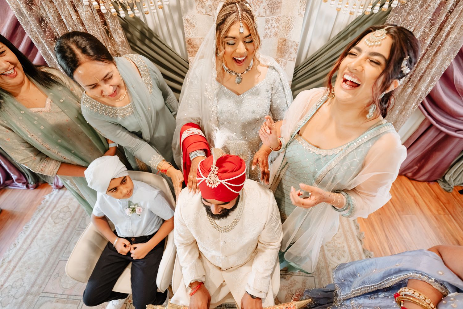 Wedding party guests in light colored outfits sitting and laughing together on floor.