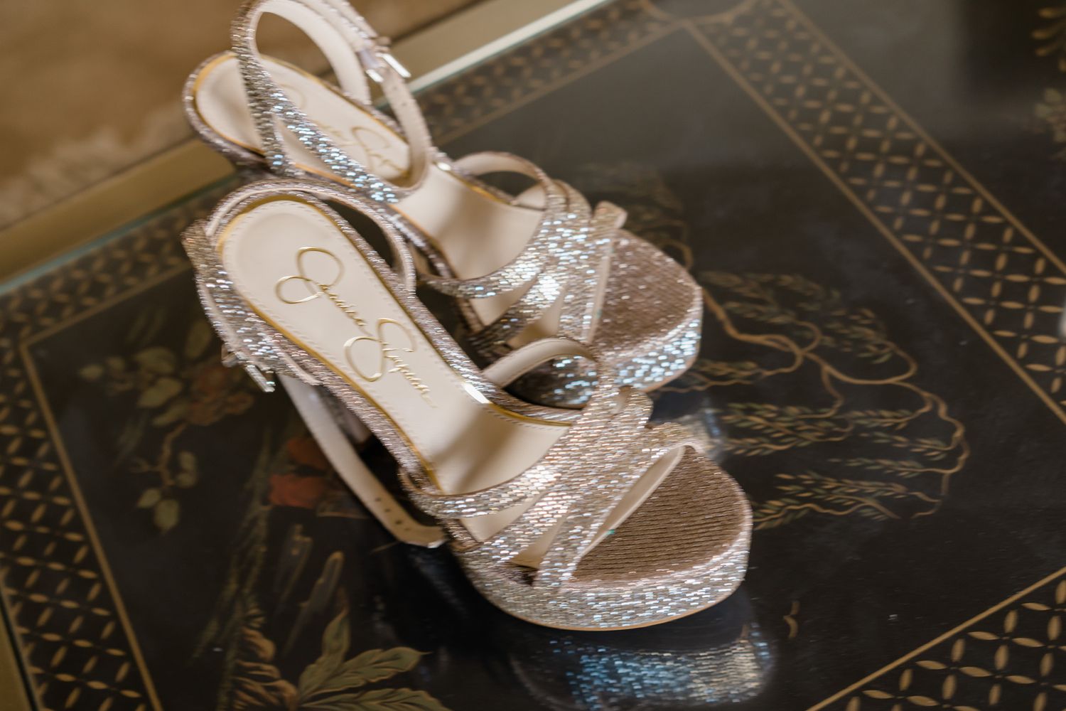 Elegant silver wedding shoes with sparkly embellishments displayed on a decorative black surface.