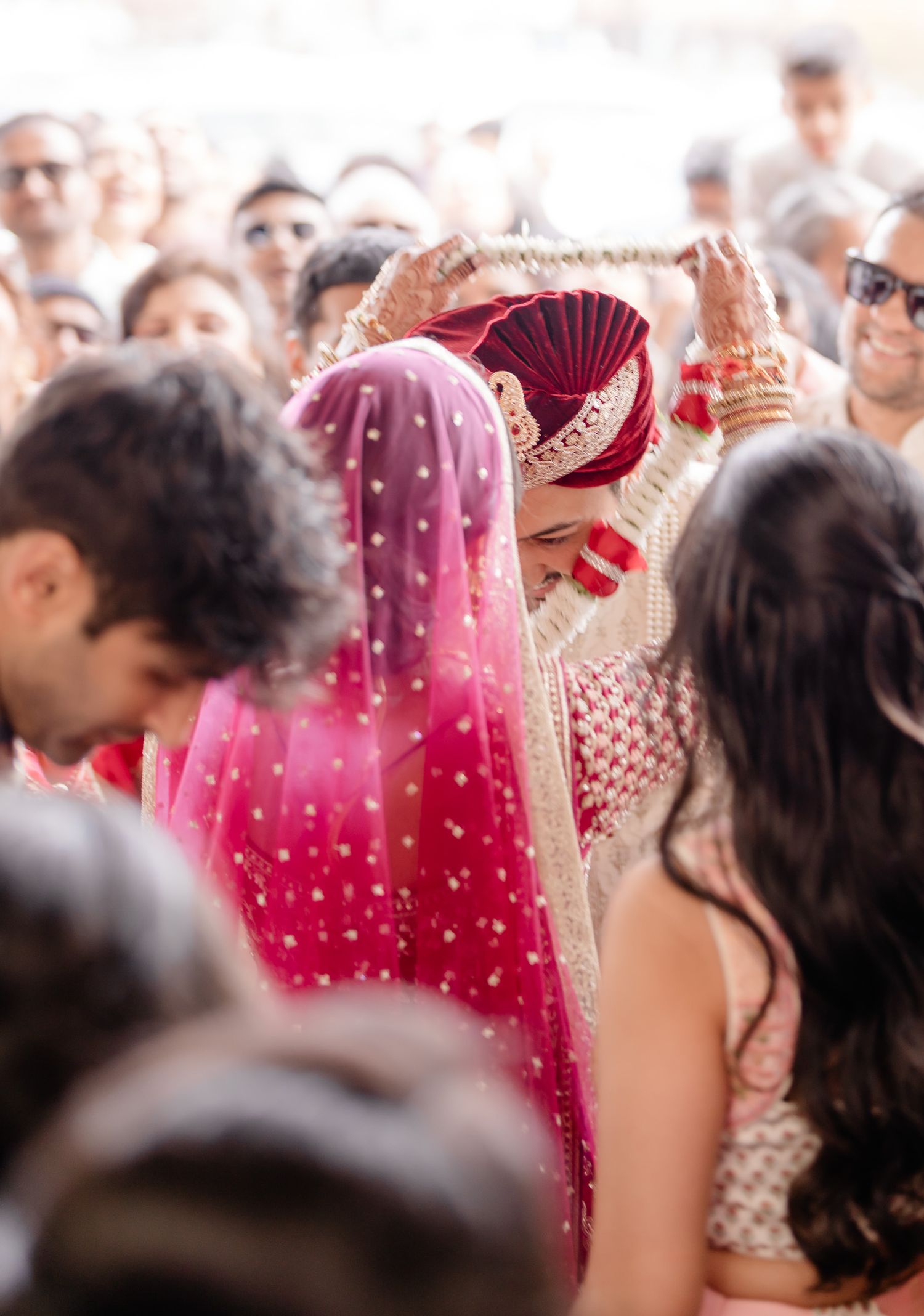 Wedding celebration crowd with traditional Indian attire featuring vibrant red and pink colors in the foreground.