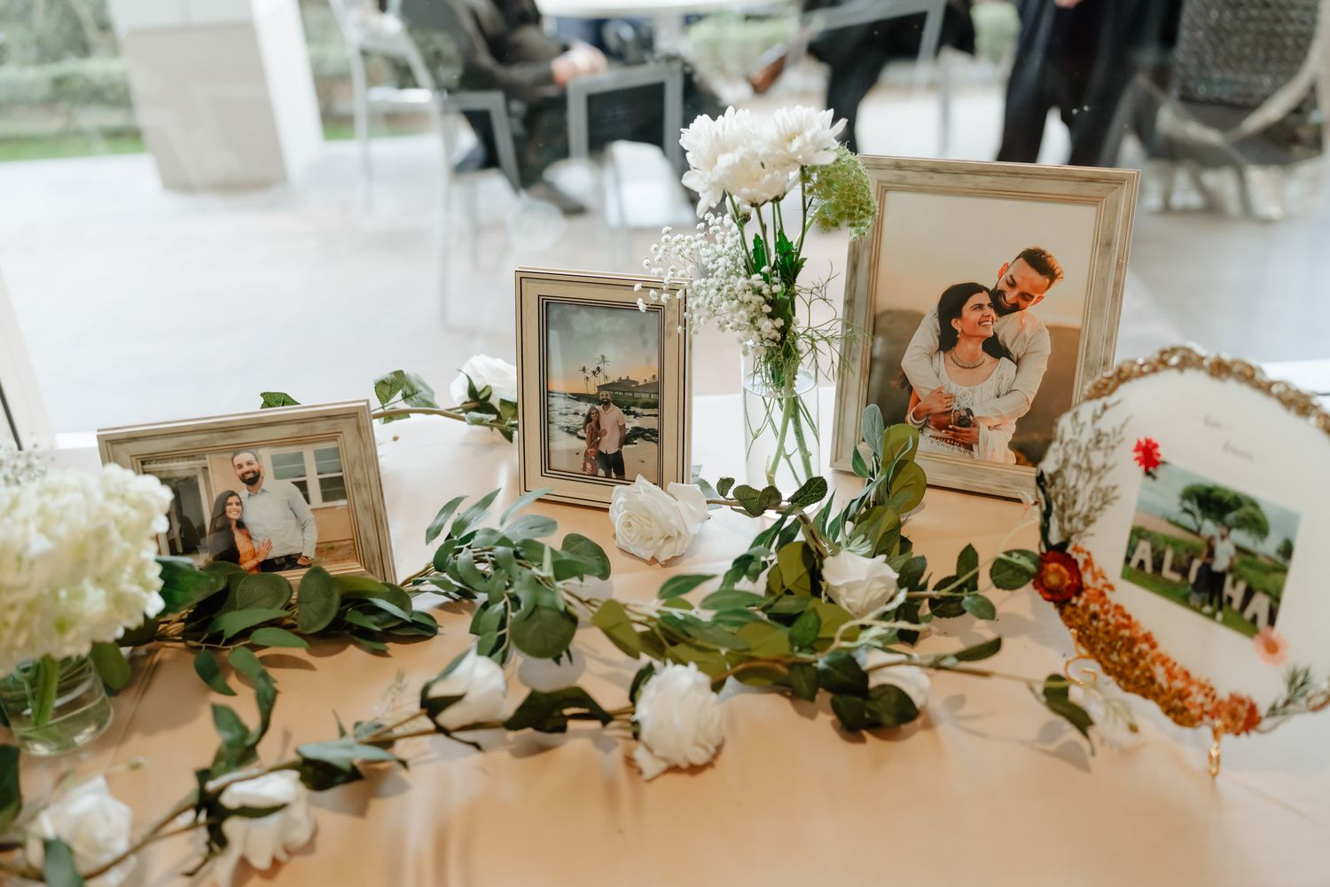 Wedding photo display table decorated with greenery garlands and framed pictures.