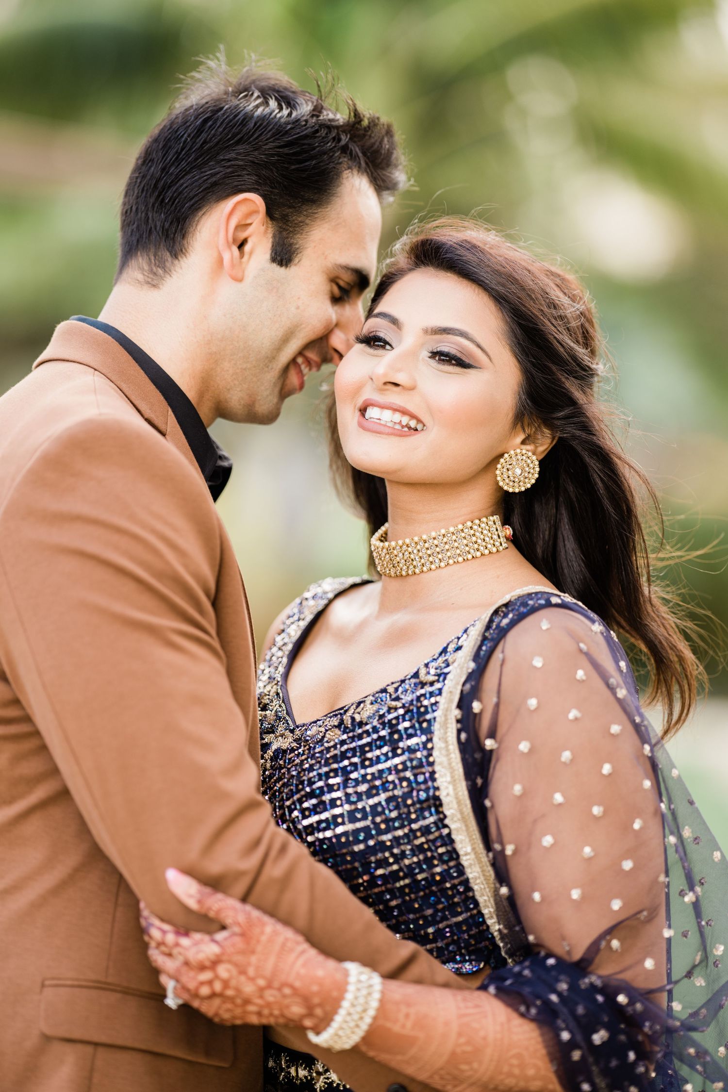 A romantic couple in formal attire shares intimate moments in a garden setting, wearing brown suit and navy dress.