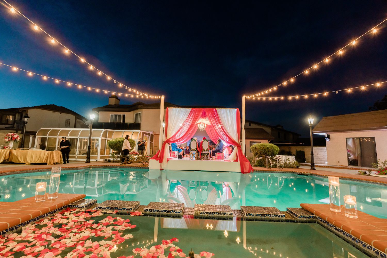 Nighttime pool party setting with string lights creating a magical ambiance over illuminated turquoise water.