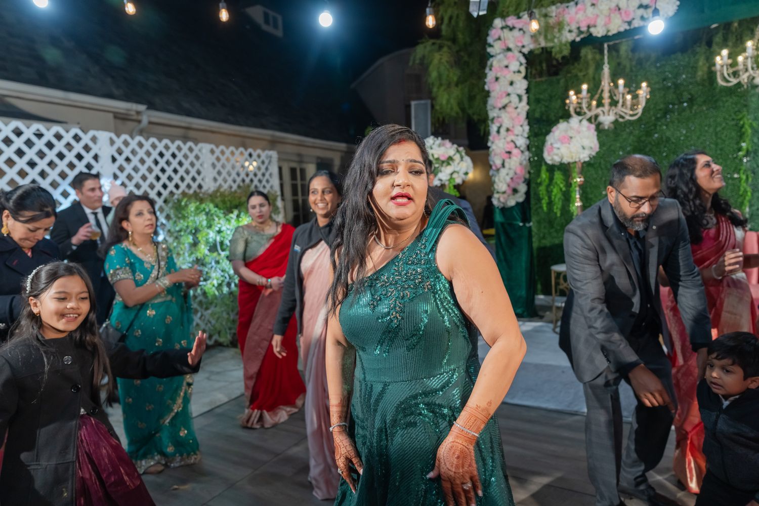 Evening wedding reception with guests dancing under string lights and floral arrangements.