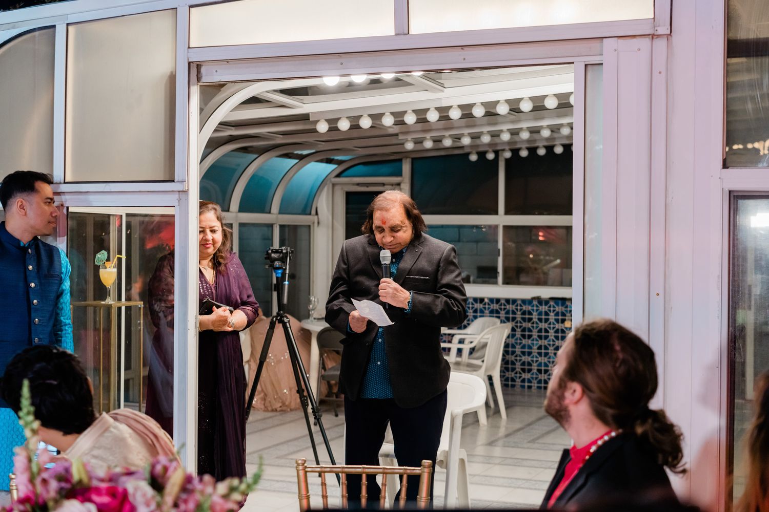 Wedding celebration inside a modern venue with large windows and elegant lighting fixtures.