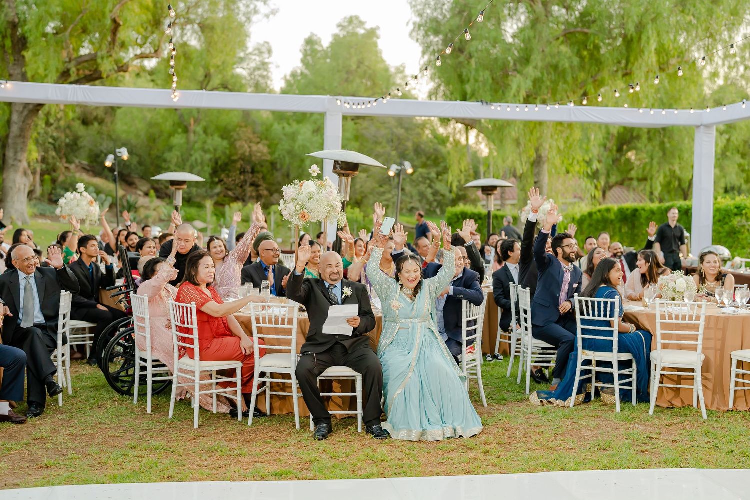 Outdoor wedding ceremony setup with white chairs and guests seated under trees.