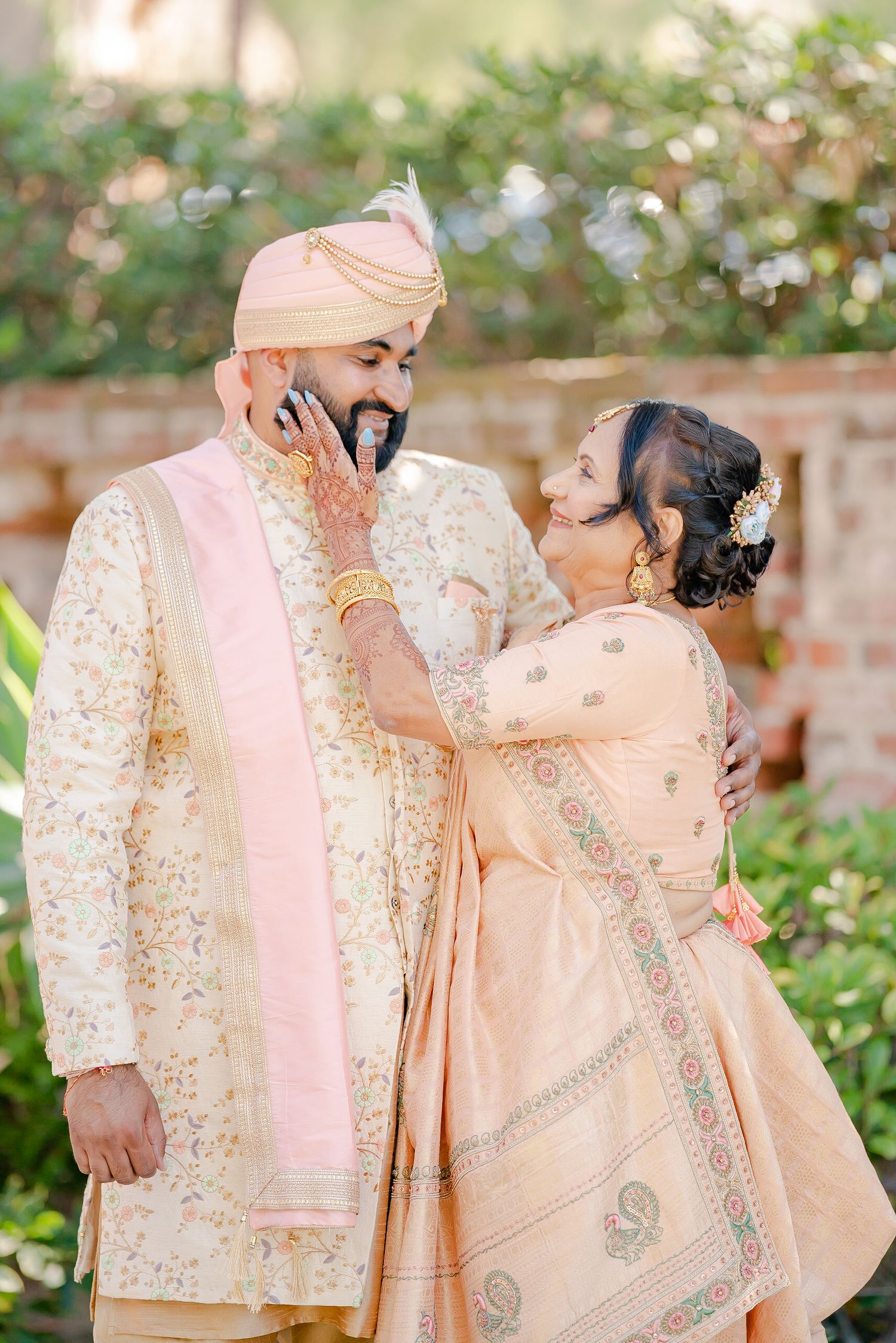 Elegant couple in traditional Indian wedding attire with cream and pink embroidered outfits in garden setting.