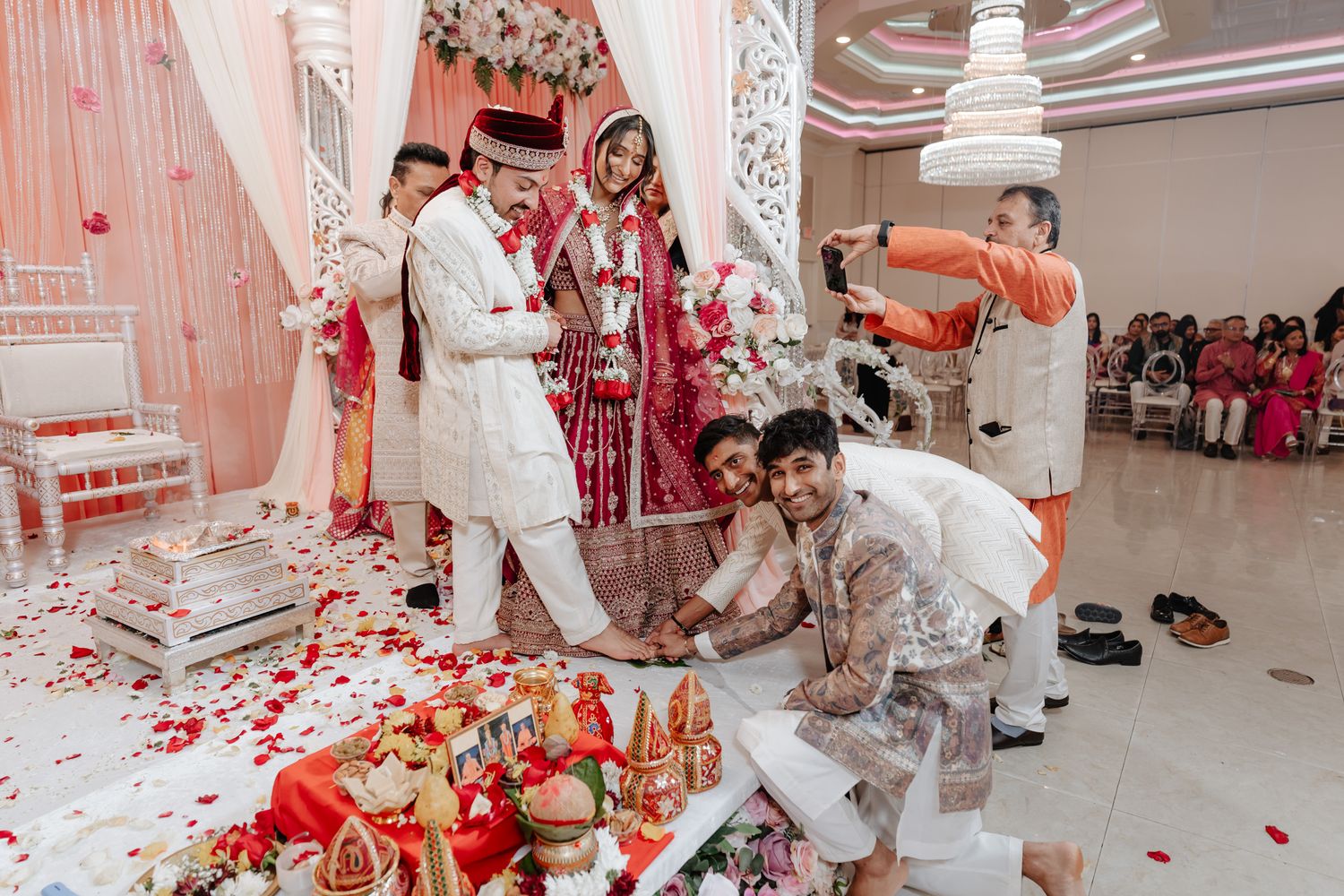 Wedding celebration with traditional Indian ceremony rituals taking place on a decorated stage with rose petals scattered around.
