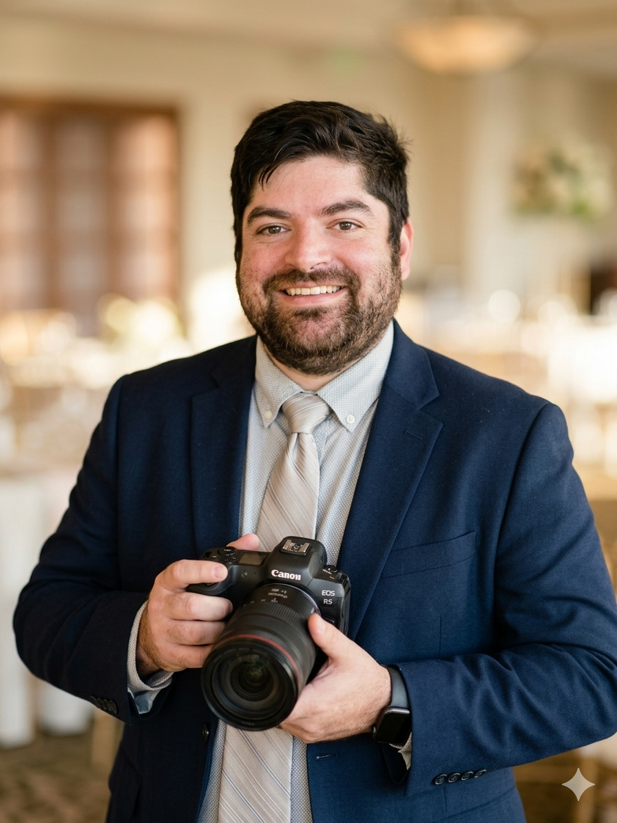 Smiling male photographer in a navy suit holding a Canon camera at an elegant wedding venue.
