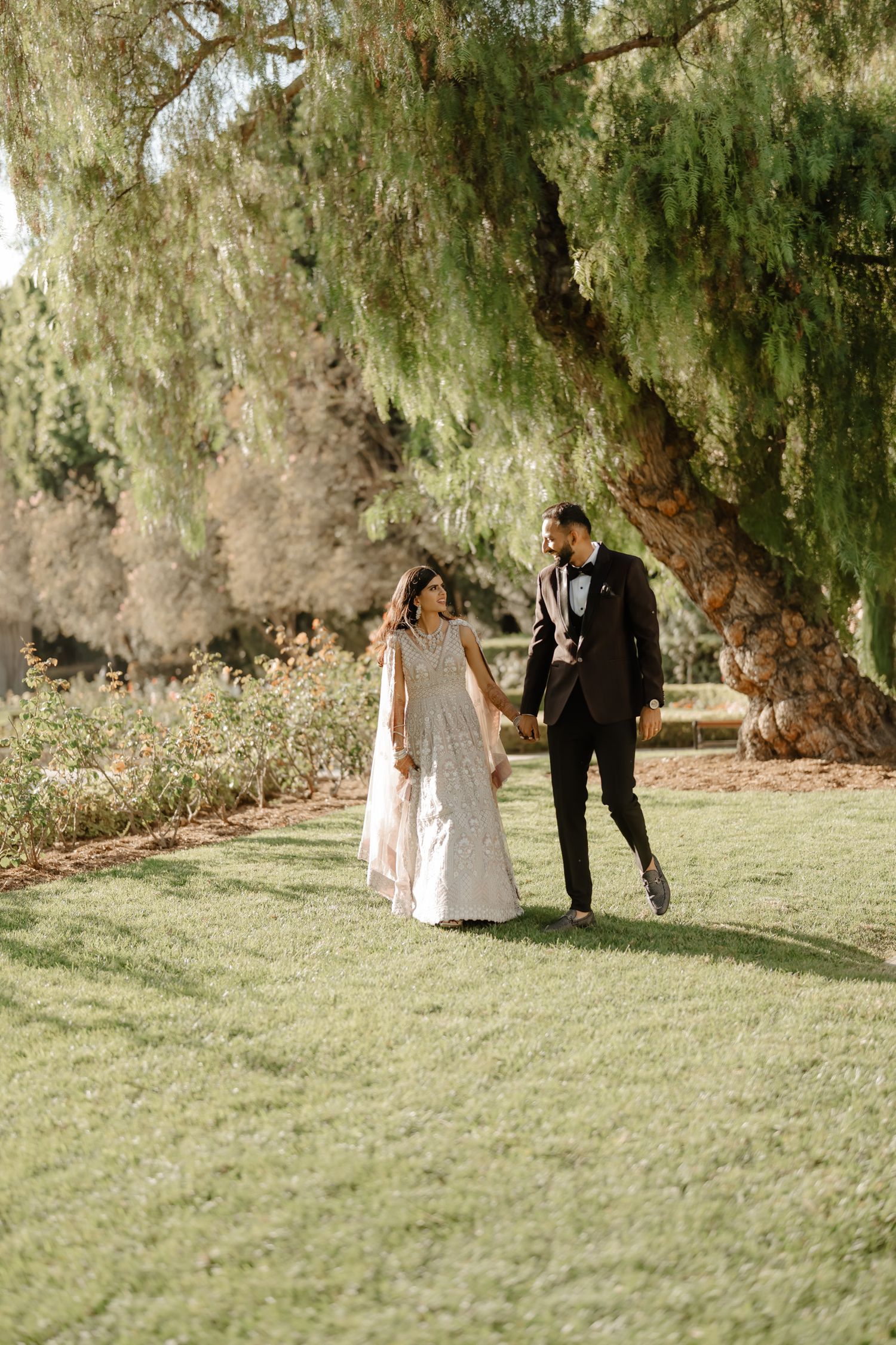 A couple poses for romantic wedding photos on a grassy lawn with willow trees in the background.