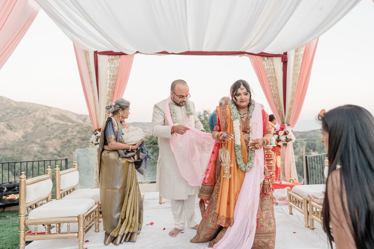 Elegant outdoor wedding setup with pink and white fabric draping and mountain views in the background.