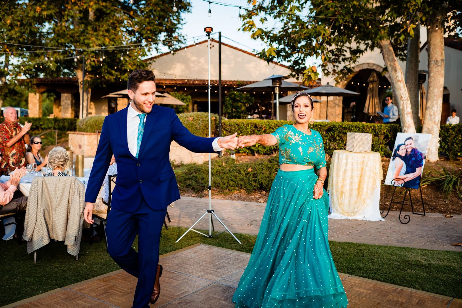A couple dances together at an outdoor wedding reception surrounded by trees and decorations.
