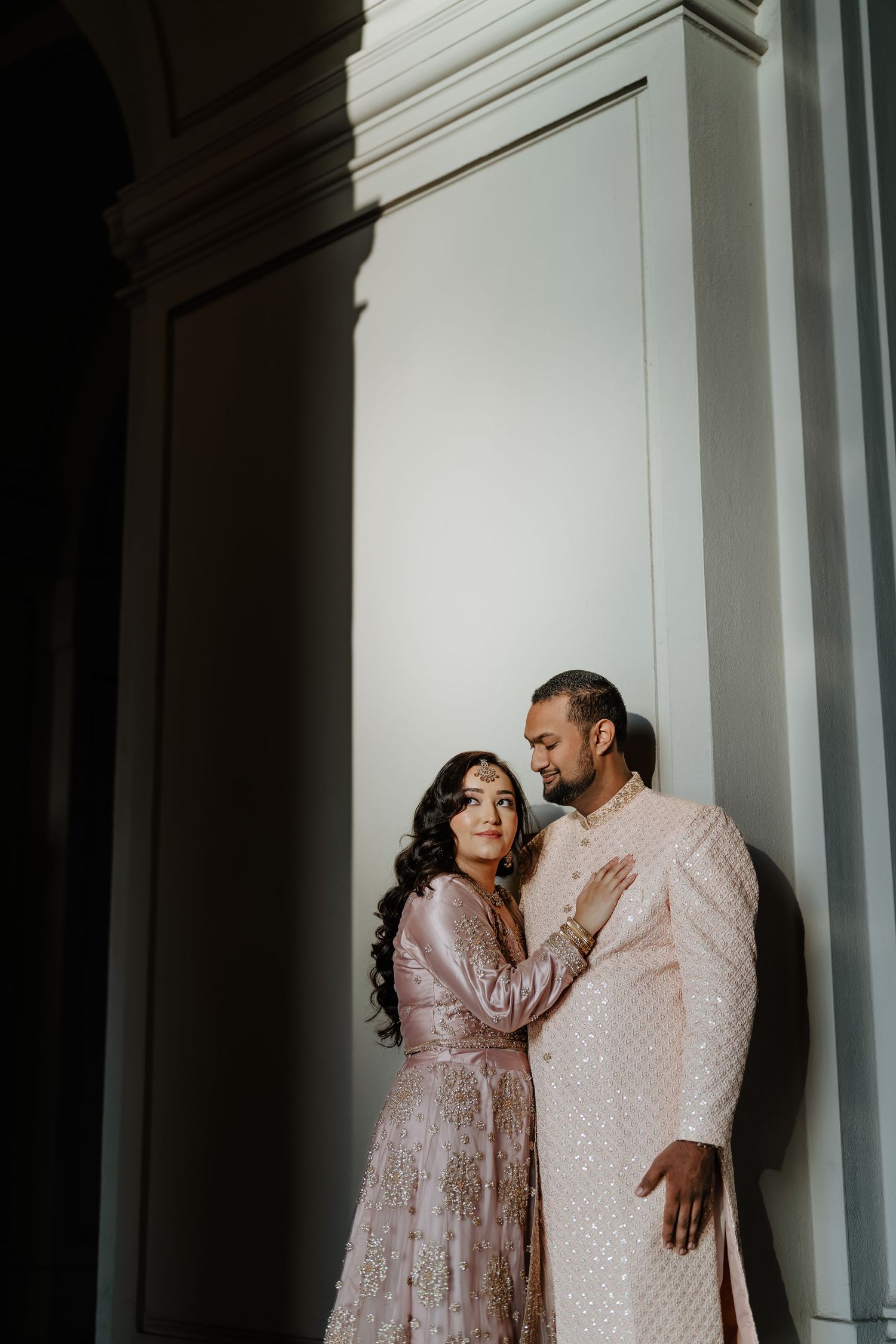 A couple in matching cream outfits share an intimate moment against a white wall.