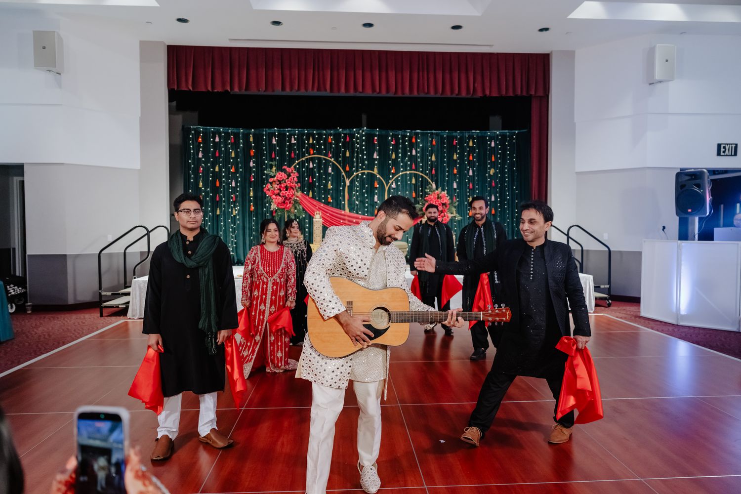 A wedding reception hall setup with red curtains and stage decorations visible in a panoramic view.