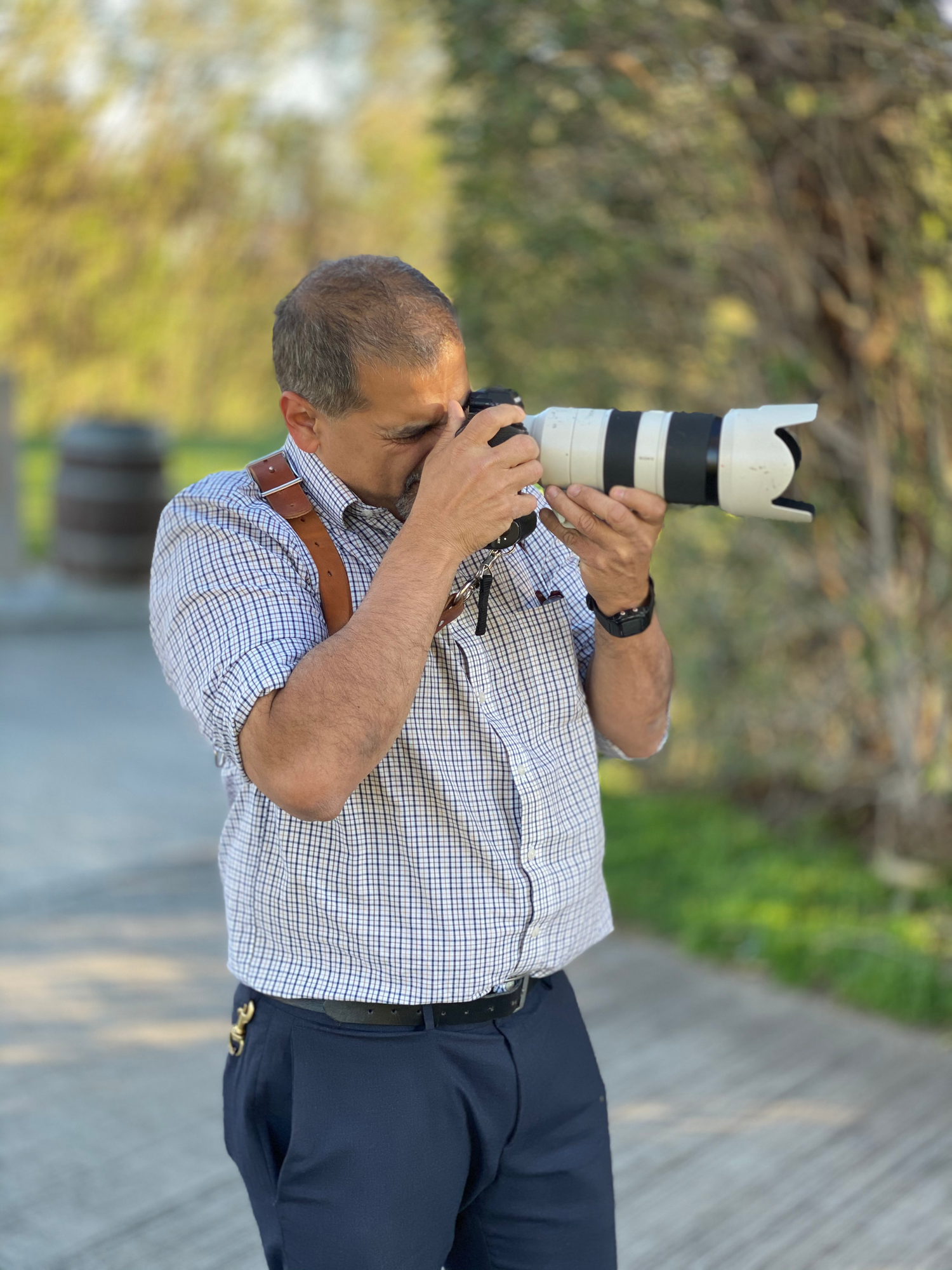 Middle-aged man photographing outdoors with a Canon camera and long telephoto lens on a sunny day.