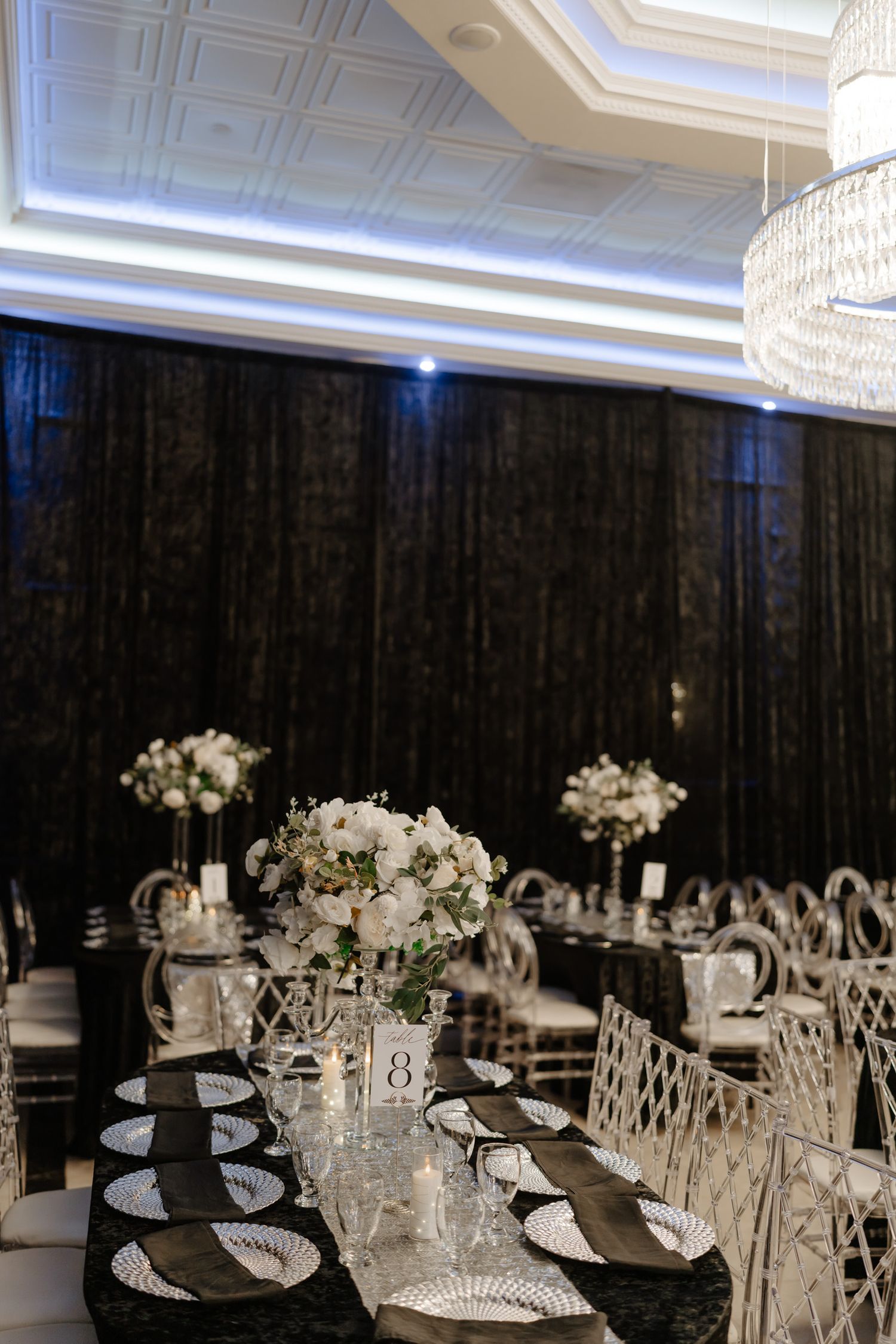 Elegant wedding reception tables set with black chargers, crystal glassware, and white floral centerpieces in a grand ballroom.