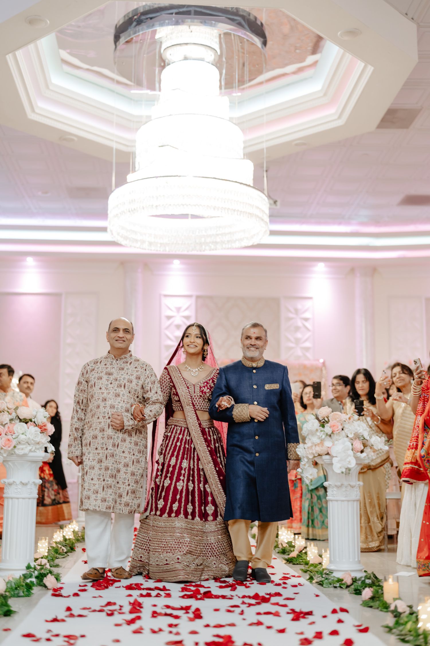 Wedding ceremony aisle decorated with rose petals and guests lining both sides in an elegant ballroom.