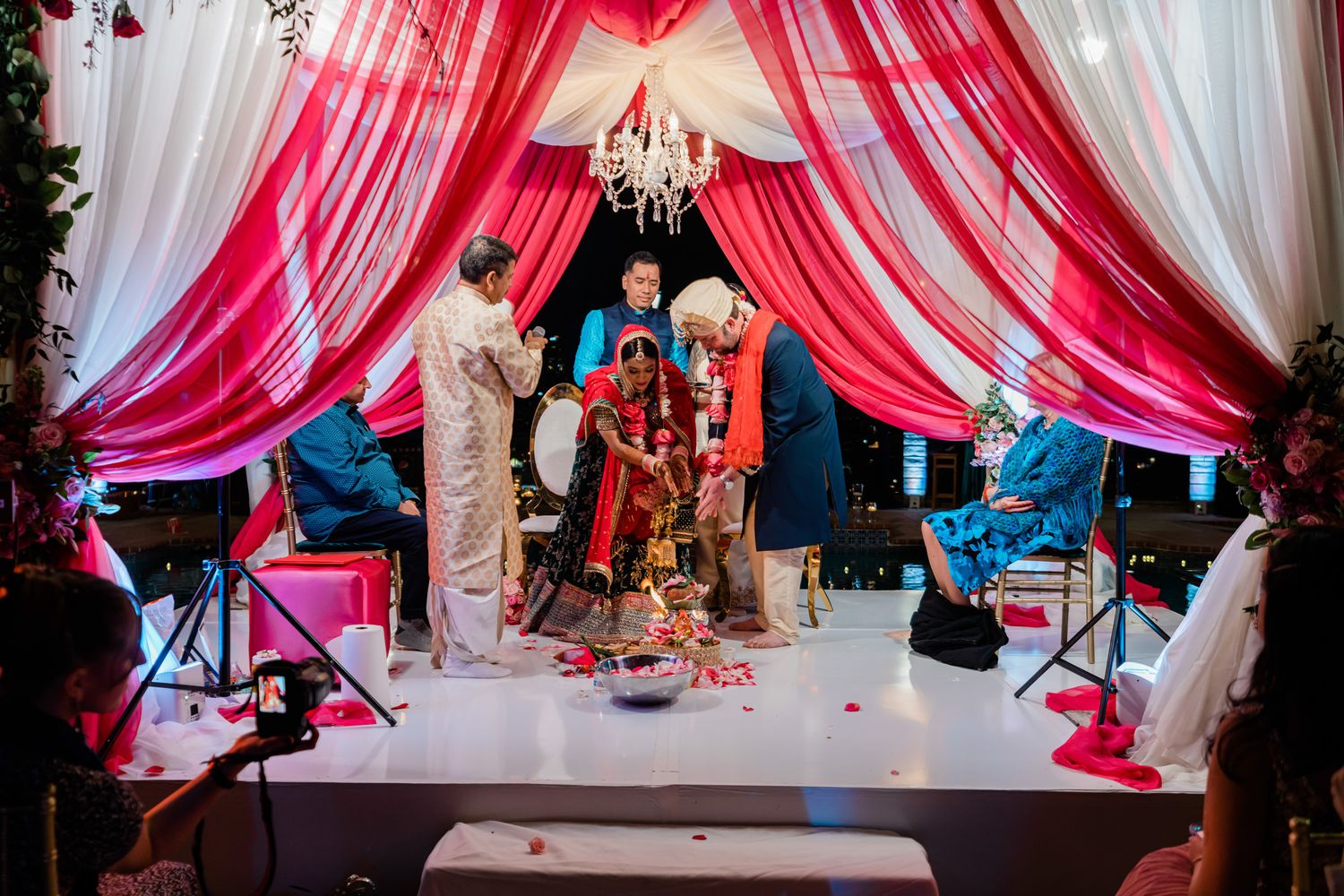 Pink and white draped fabric creates an elegant wedding reception backdrop with crystal chandeliers and floral decor.