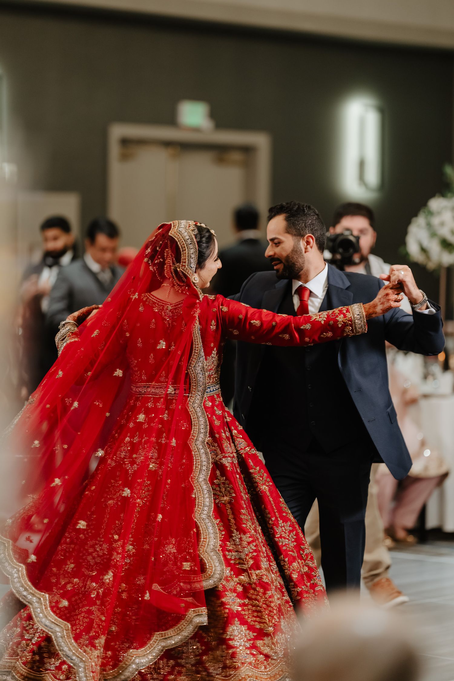 Wedding guests dance in a circle holding hands while bride in red lehenga joins celebration.