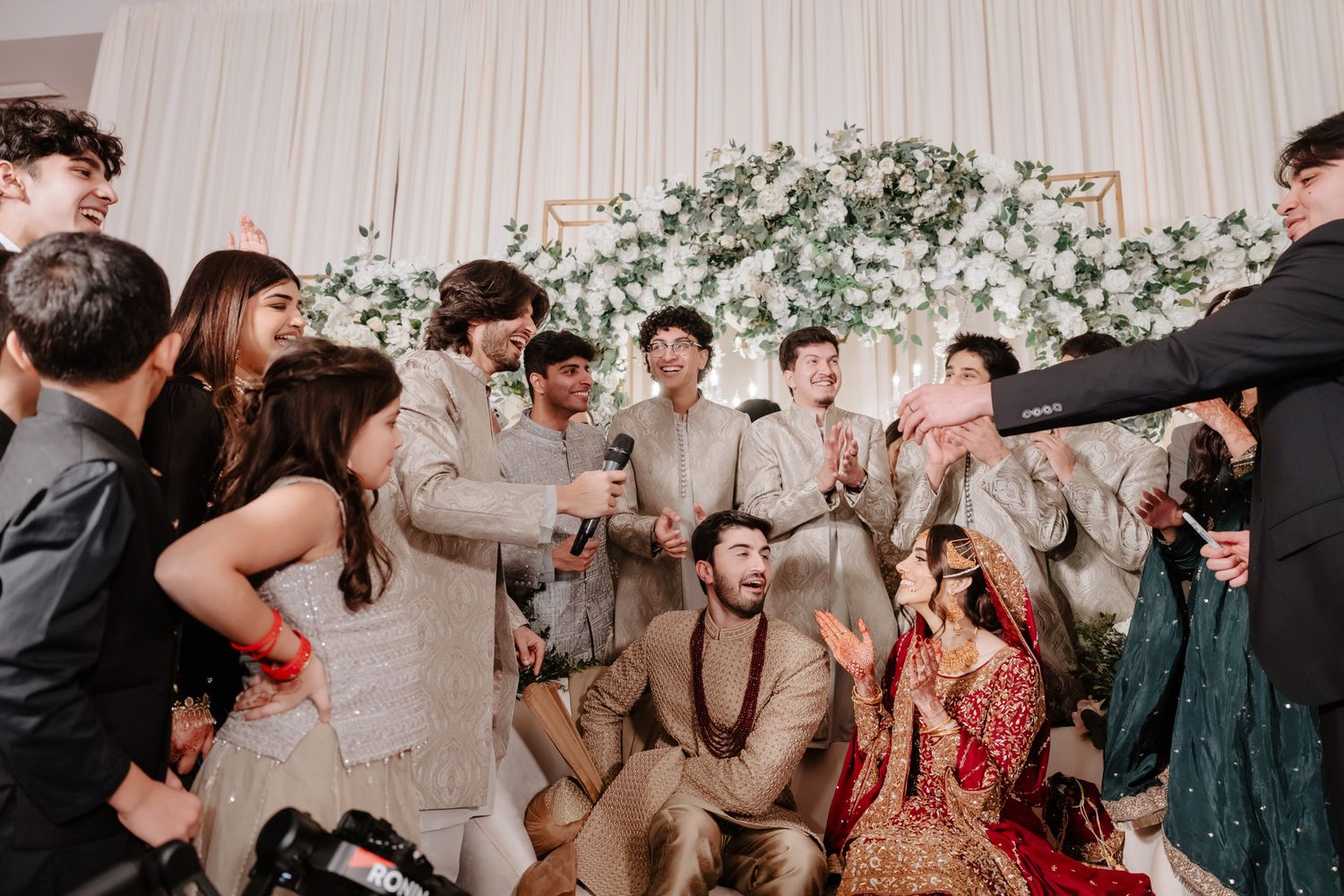Wedding guests dancing and celebrating at a lively reception with floral decor in the background.