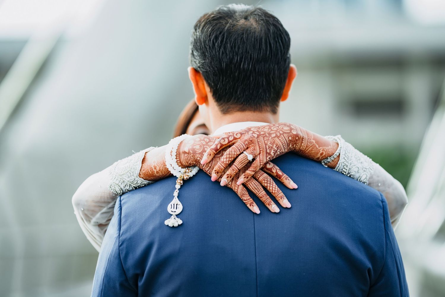 Elderly hands rest on shoulders of someone wearing a blue medical uniform from behind.