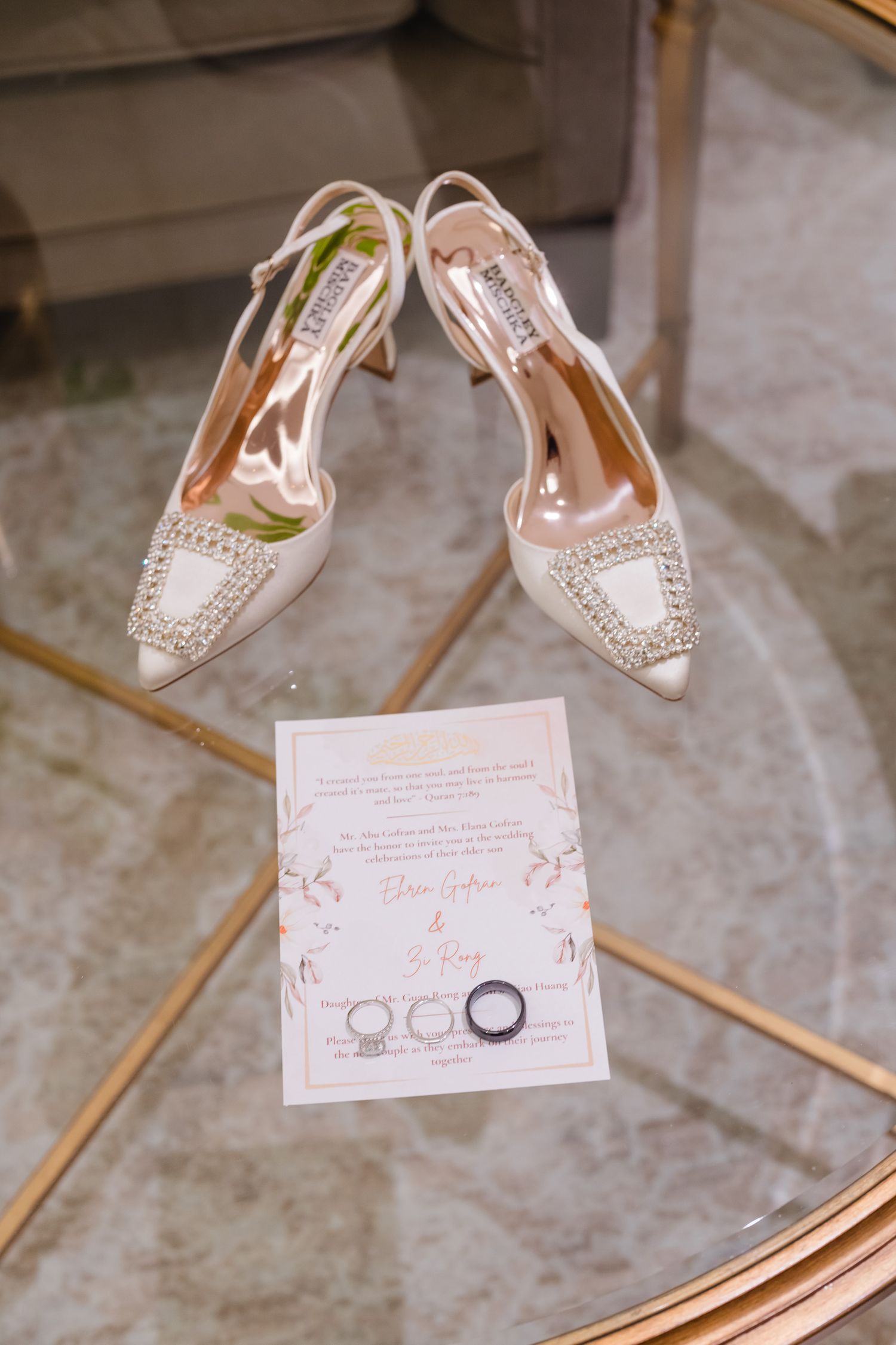 Elegant crystal-embellished bridal shoes displayed with wedding rings and invitation on a metallic surface.