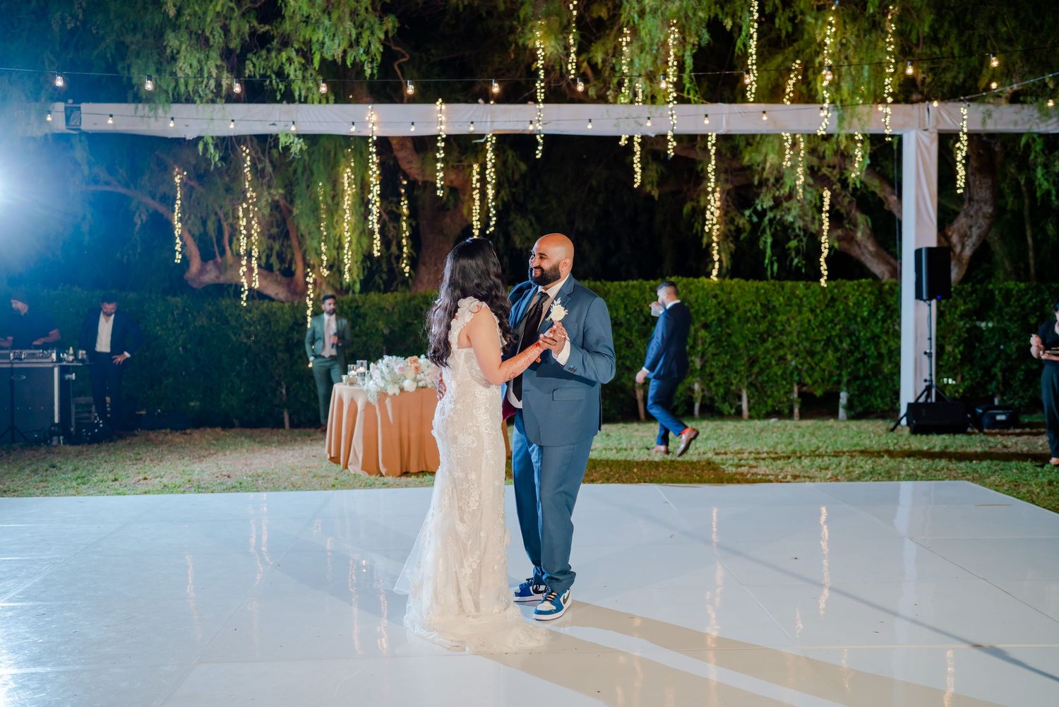 A couple shares their first dance on an illuminated outdoor dance floor under a pergola at night.