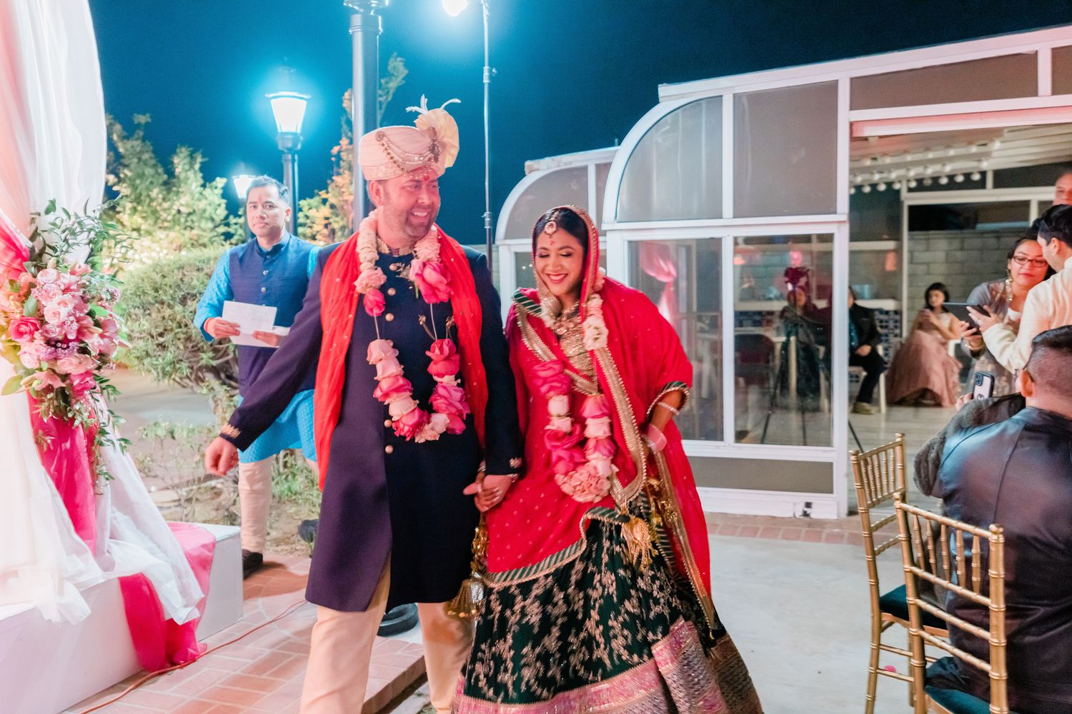 Wedding guests dance and celebrate at an outdoor reception under string lights and glowing lanterns.