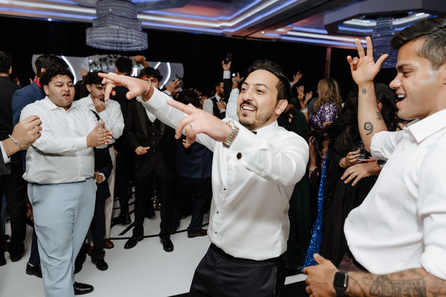 Wedding party guests dancing and celebrating with raised arms in a modern venue.