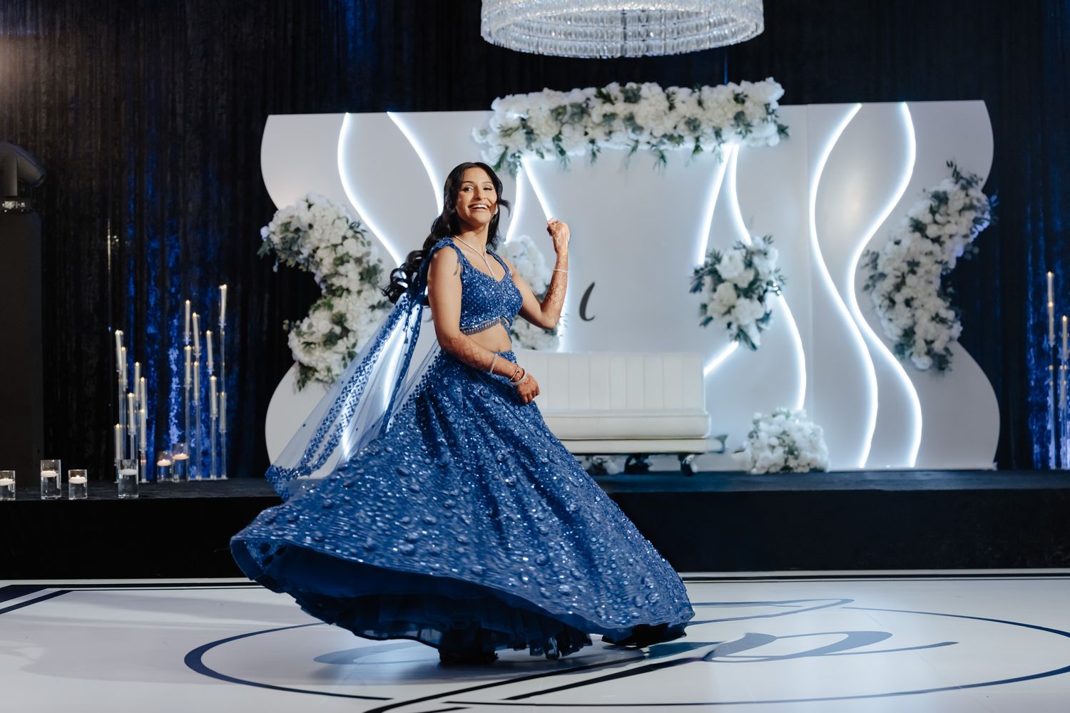 Woman in sparkling navy blue ball gown twirling on illuminated dance floor.
