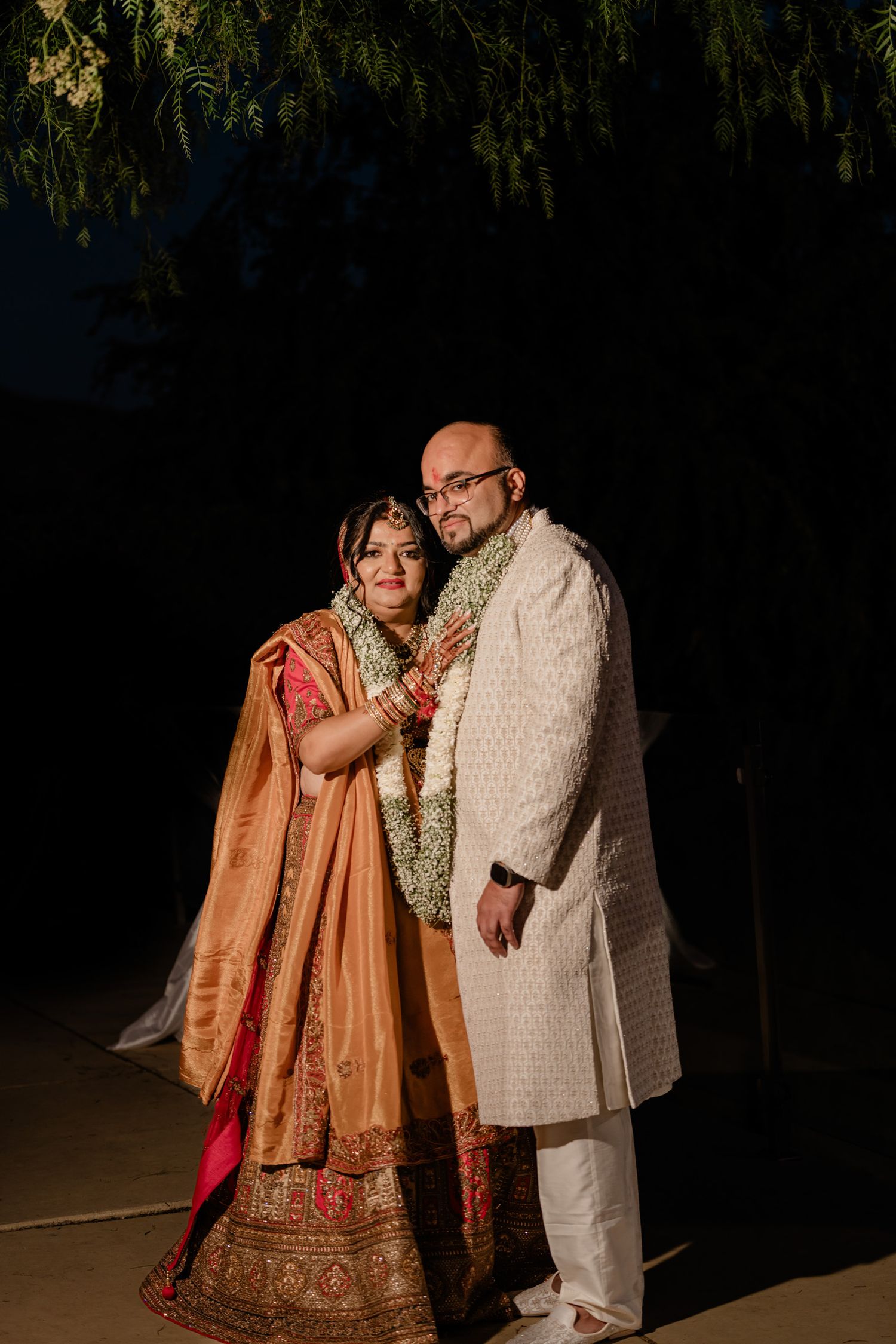Couple poses together in traditional South Asian wedding attire during an evening outdoor photoshoot.