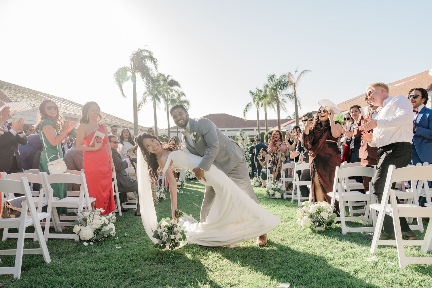 Wedding guests seated in white chairs on manicured lawn during outdoor ceremony.