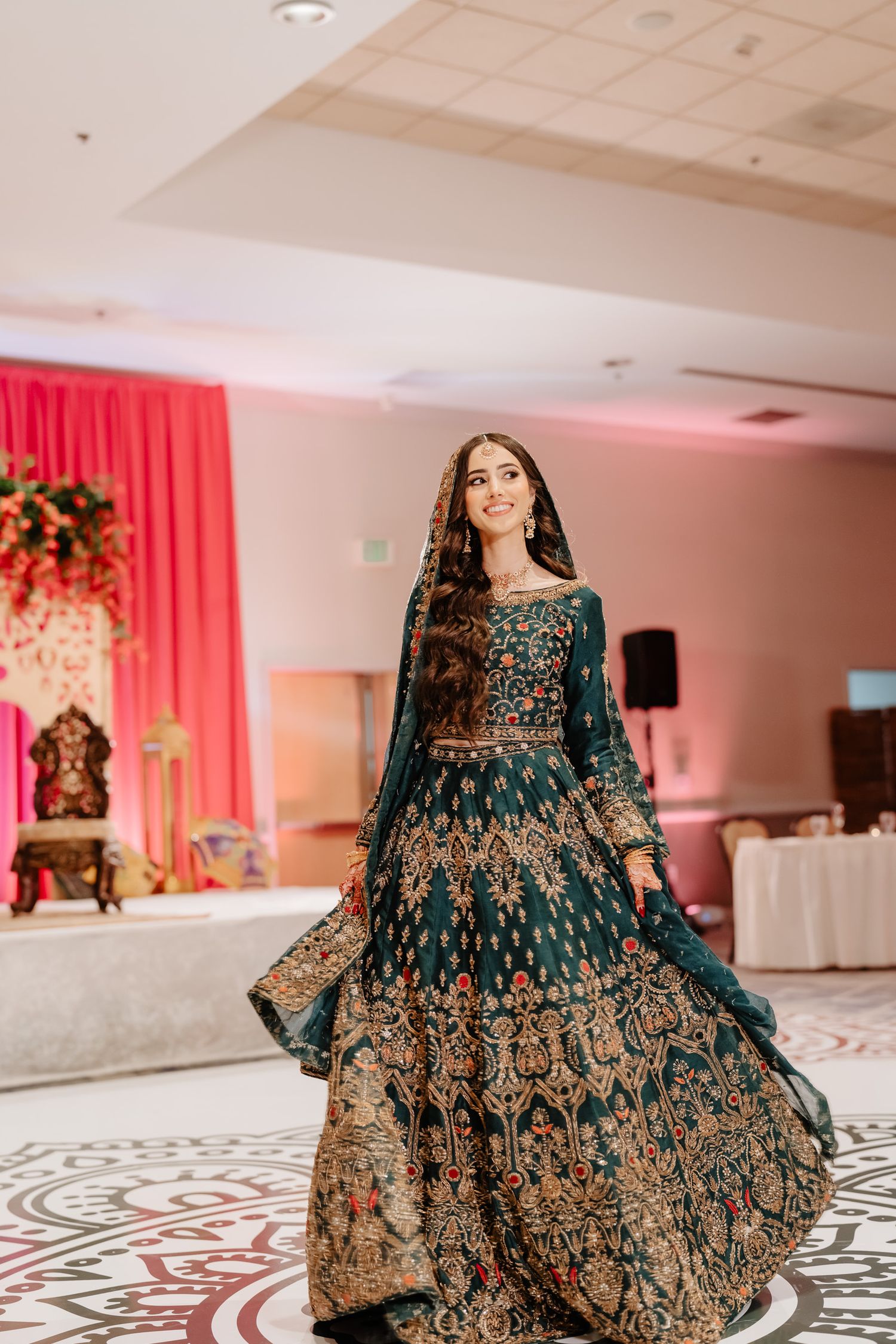 Stunning dark green and gold lehenga with intricate embroidery twirls on marble floor at wedding reception.
