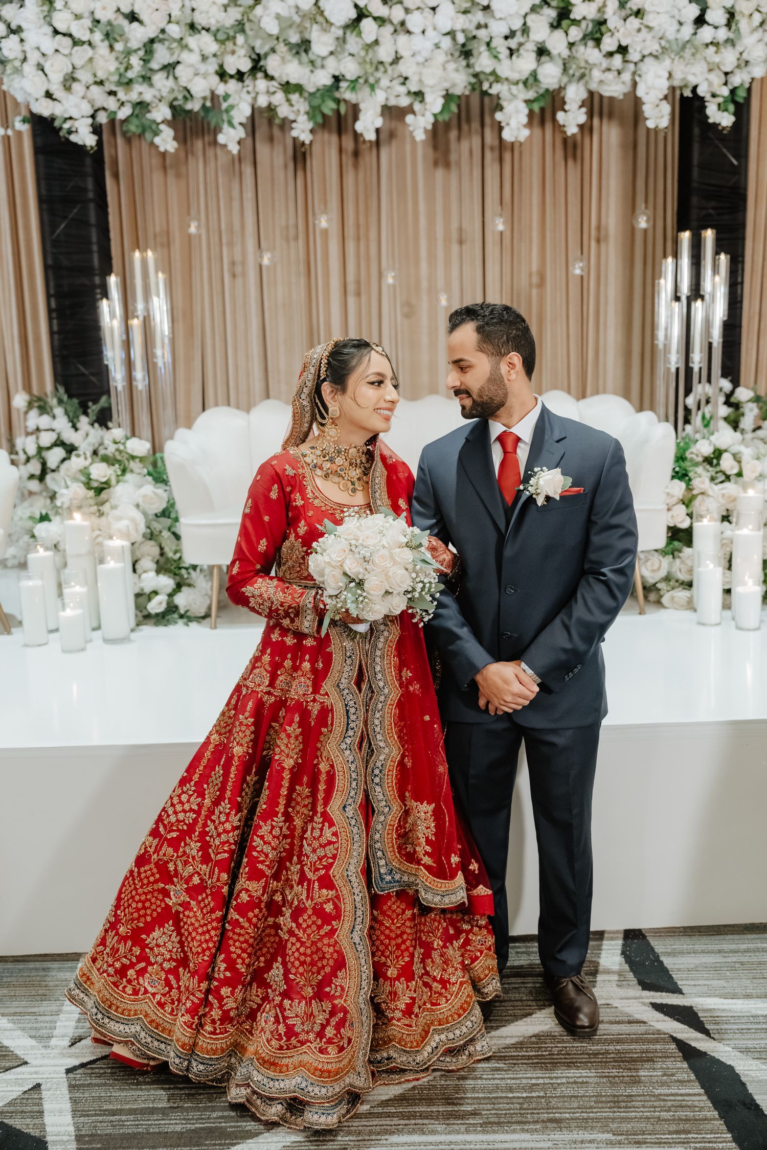 A series of romantic wedding photos showing a couple in traditional South Asian attire with red bridal lehenga against white decor.