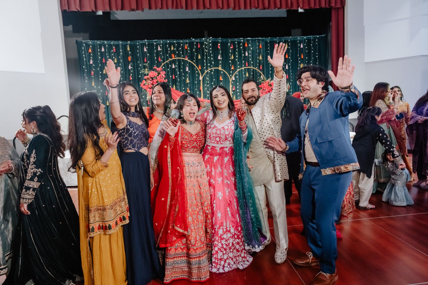 A festive Indian wedding celebration with guests in colorful traditional attire gathered in a large venue.