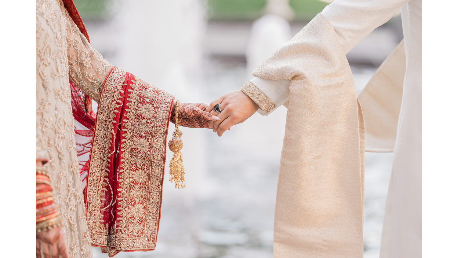 Traditional Indian wedding ceremony details with hands exchanging rings and holding decorative items in rich red and gold.