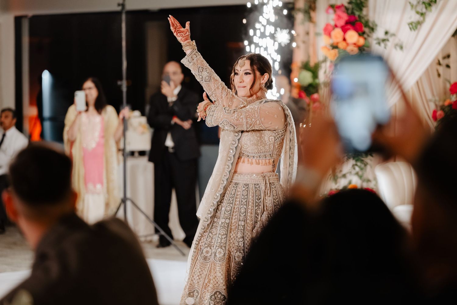 Bride in embellished lehenga dancing gracefully at an Indian wedding reception with guests watching.