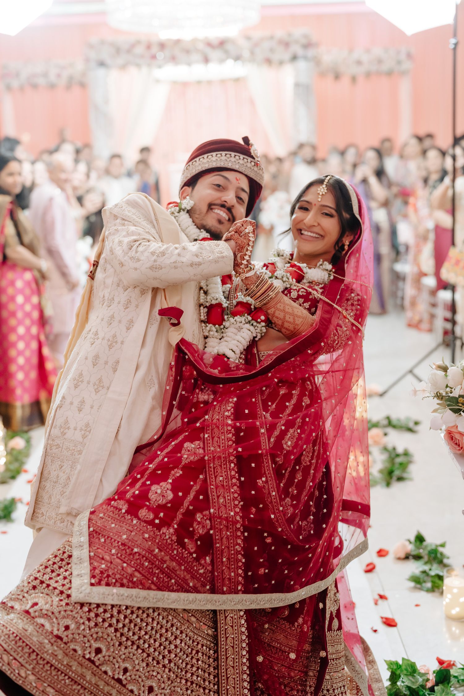 Joyful wedding celebration with couple in traditional Indian attire dancing among rose petals.