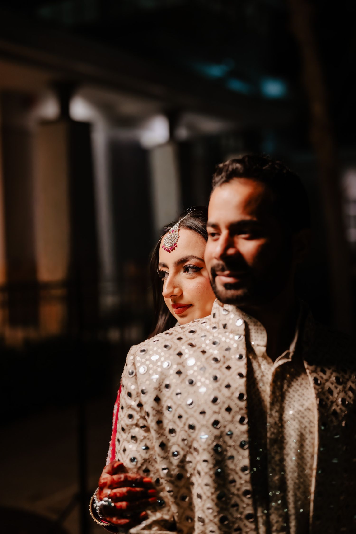A romantic couple shares an intimate moment in traditional South Asian wedding attire with polka dot and embroidered details.