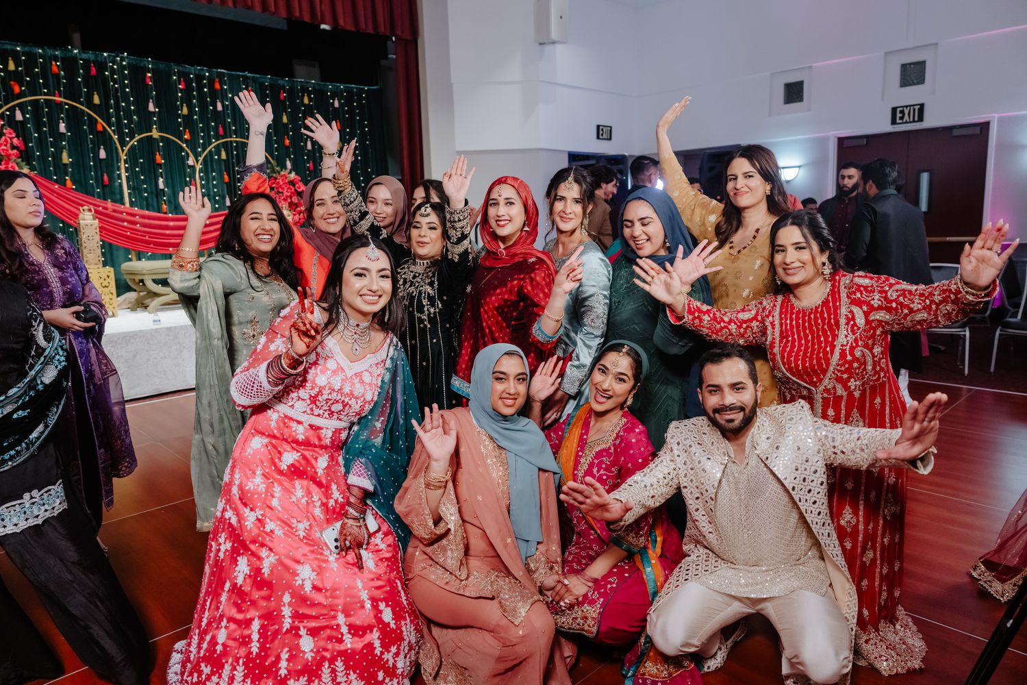 Joyful group photo of wedding guests in traditional South Asian attire celebrating on dance floor.