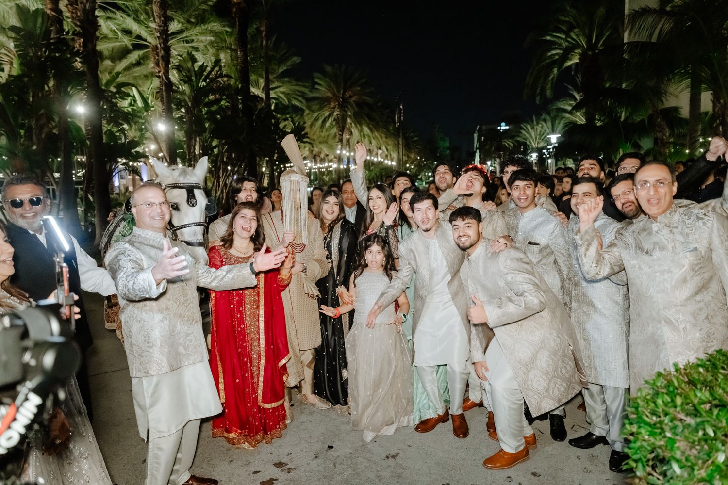 Wedding party guests dressed in white gather outdoors for a festive celebration at night.