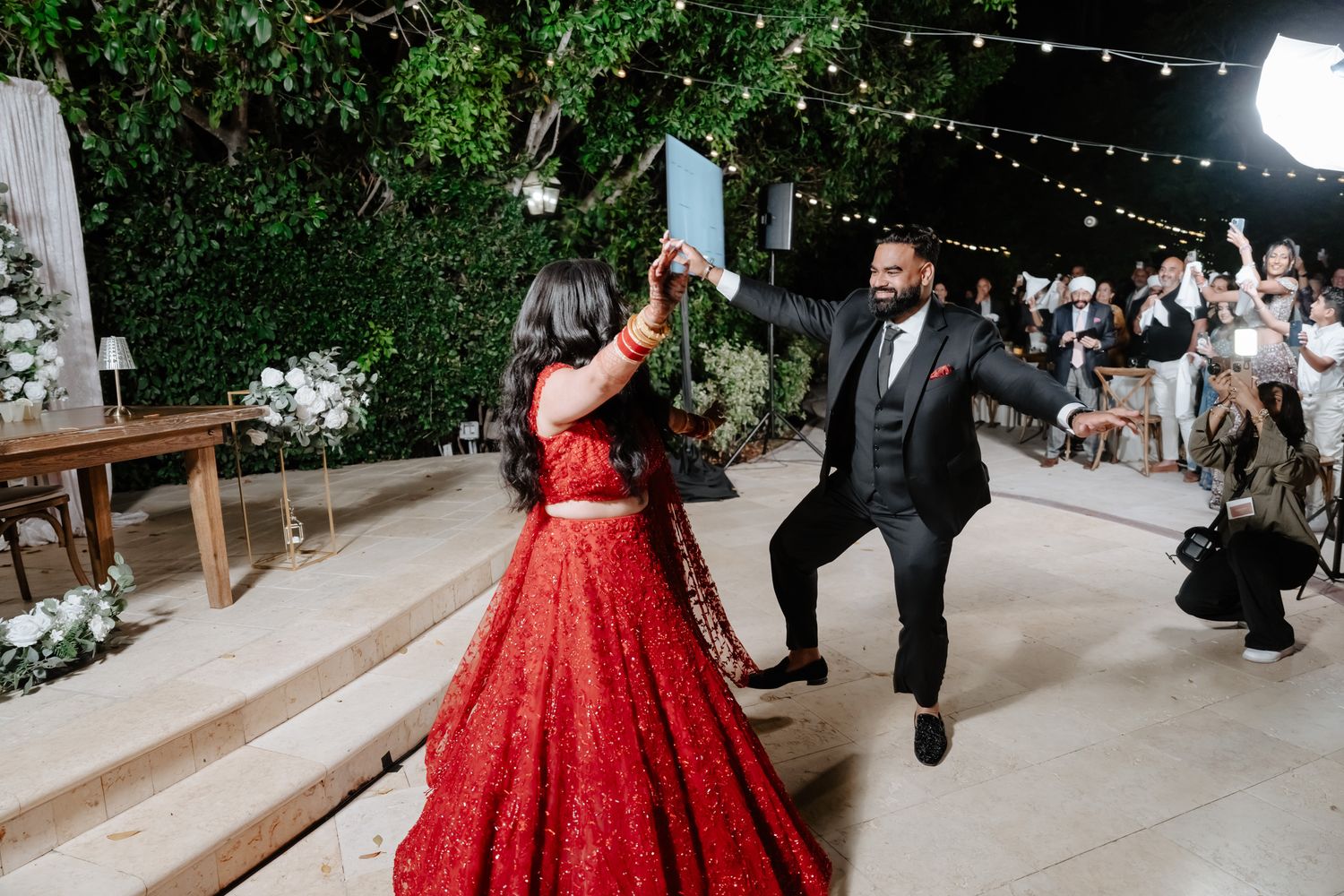 Dancing couple celebrates on an outdoor patio decorated with string lights and greenery.