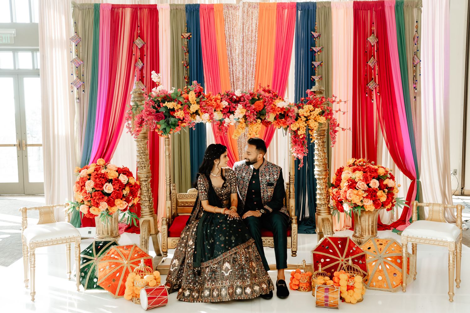 Colorful fabric drapes and floral decorations create stunning wedding venue backdrop.